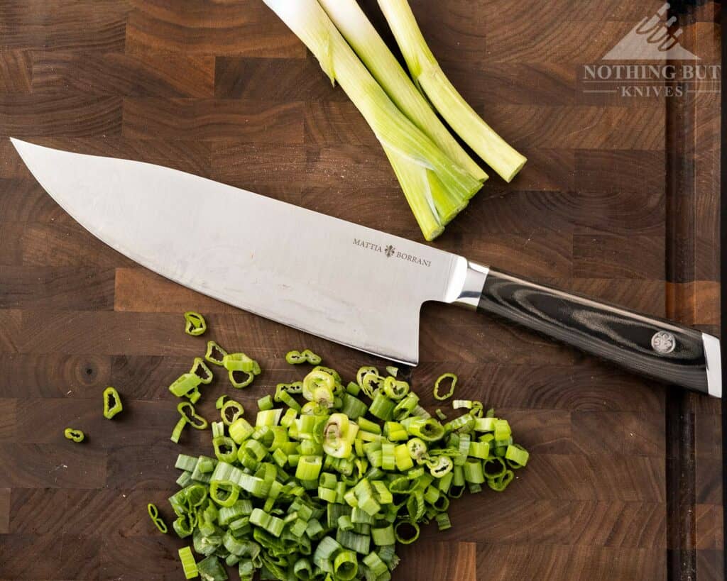 The Mattia Borrani Bowie chef knife on a cutting board with chopped green onions.