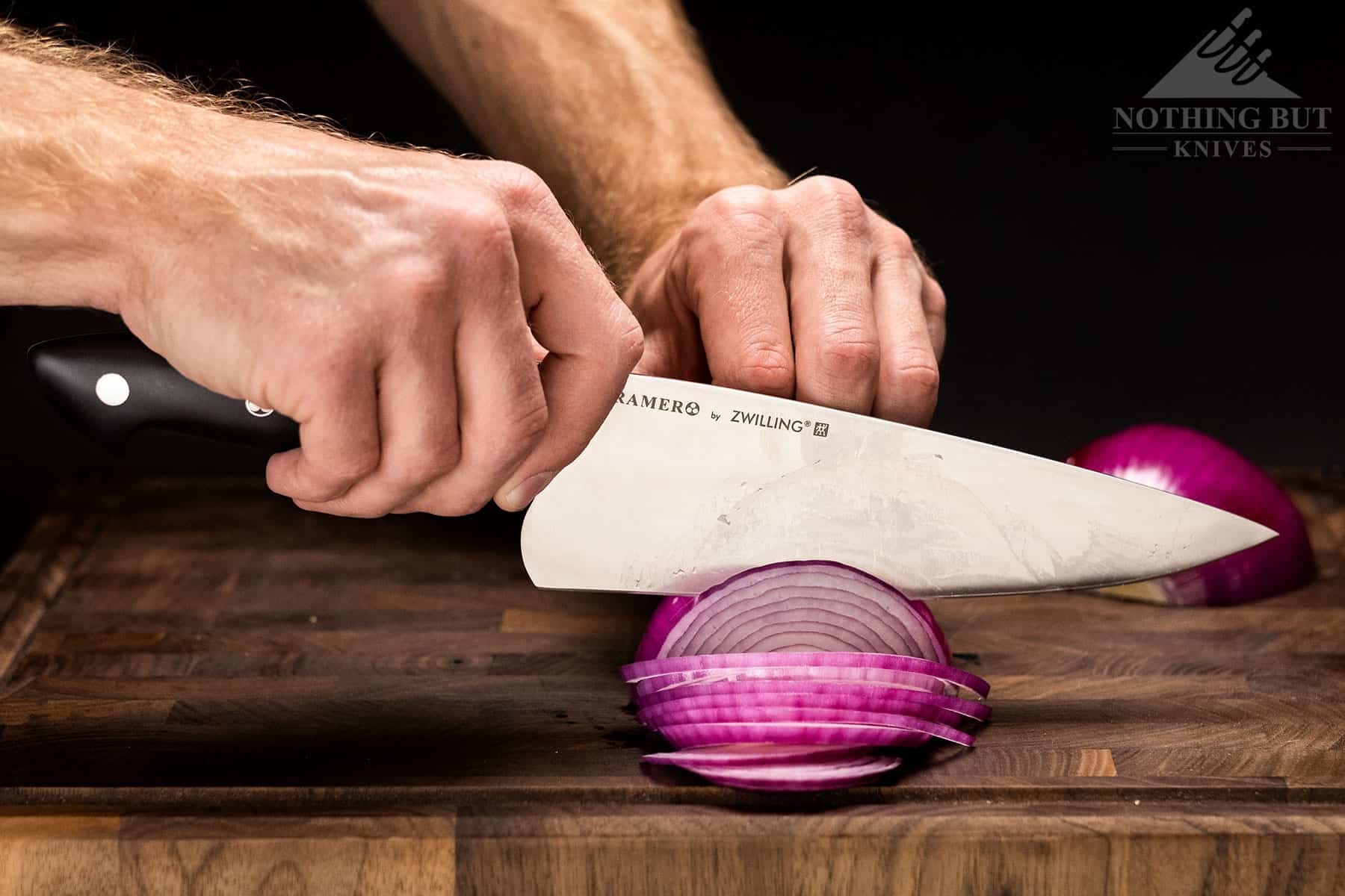 Utilizing the pinch grip while slicing a red onion with a Zwilling Kramer chef knife.