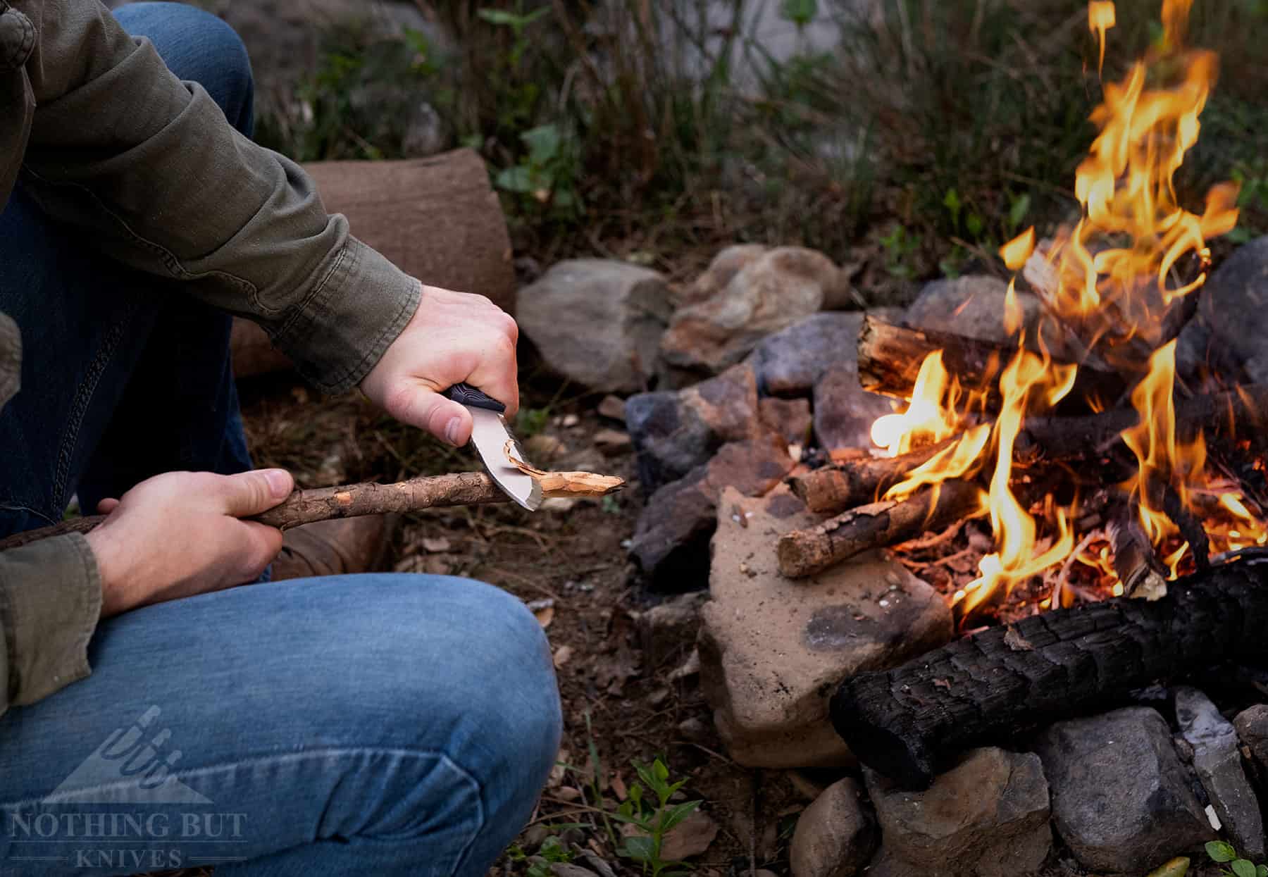 Off Grid Ridgeback Review - Image 12 A close up of a person carving a stick next to a campfire to show how effective the scandi grind on the Ridgeback is.