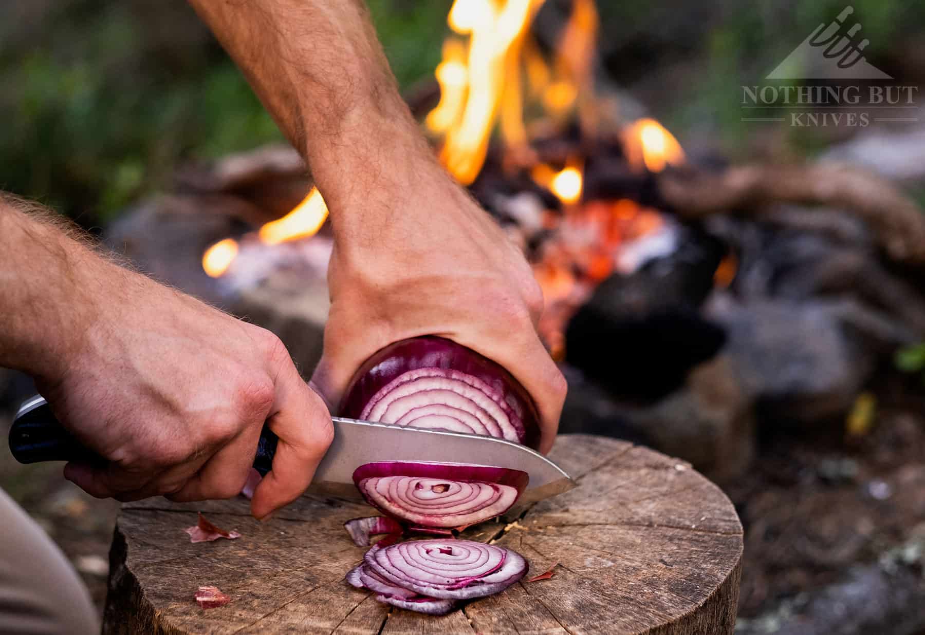 A close-up of the Ridgeback bushcraft knife being used to slice an onion by a campfire.