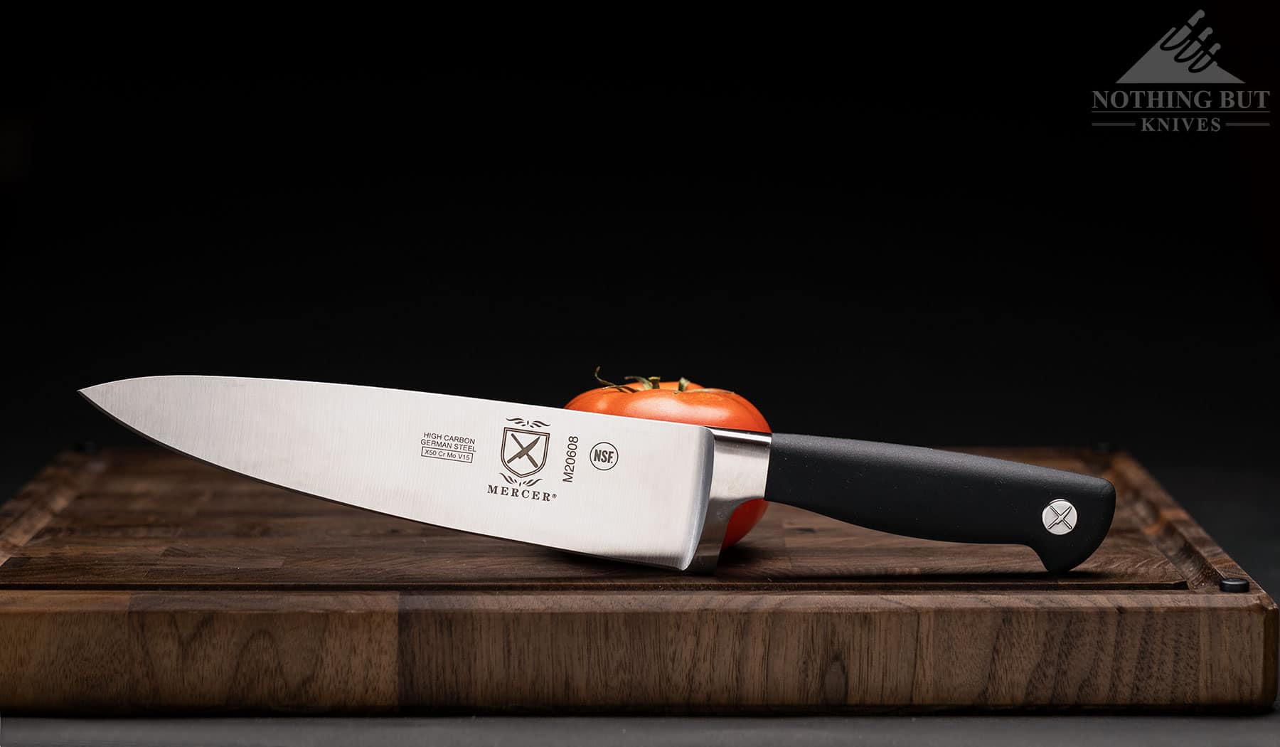The Mercer Genesis 8 inch chef knife on a cutting board with a tomato to show scale and blade profile.