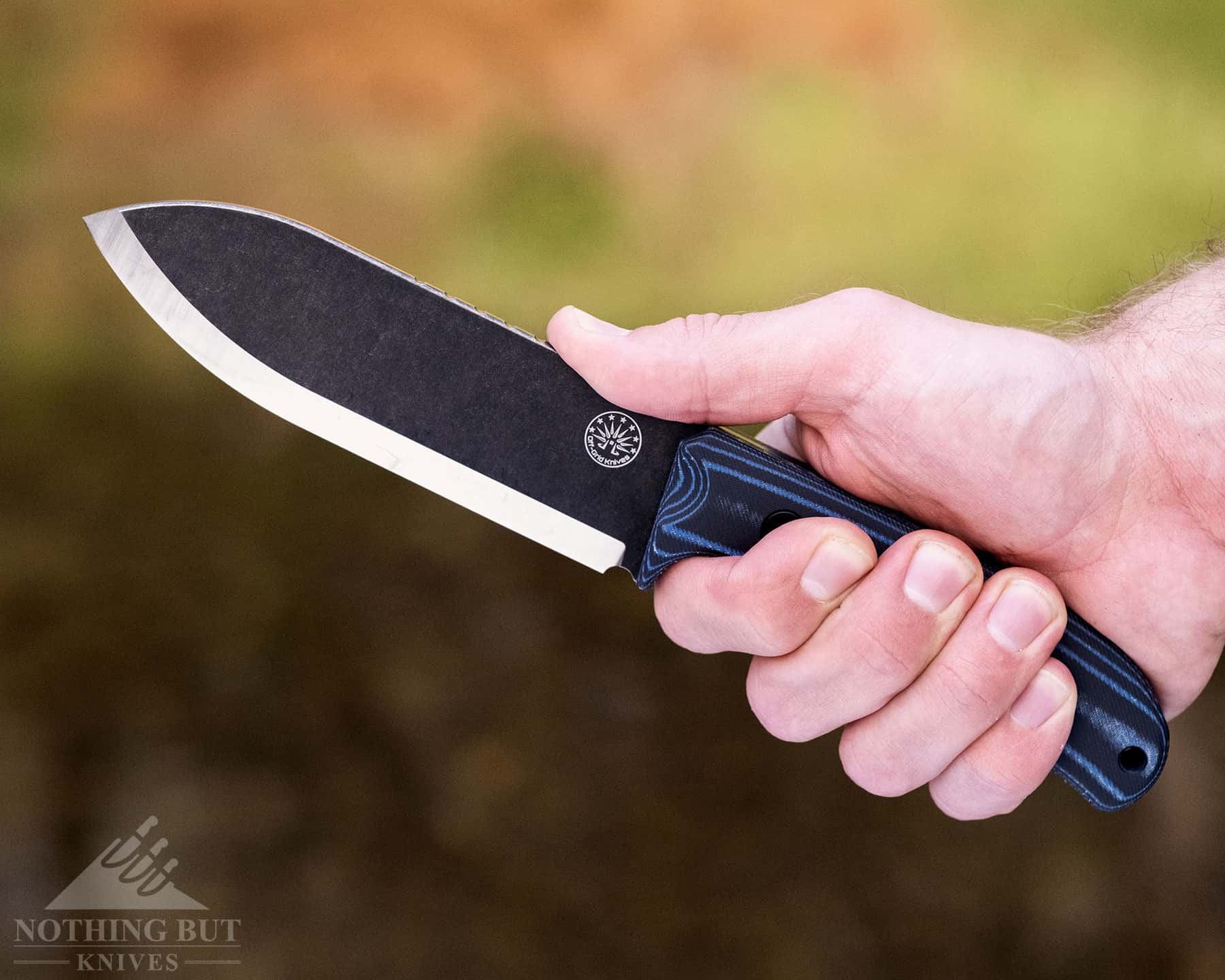 A close-up of a person's hand gripping the handle of the Ridgeback knife. 