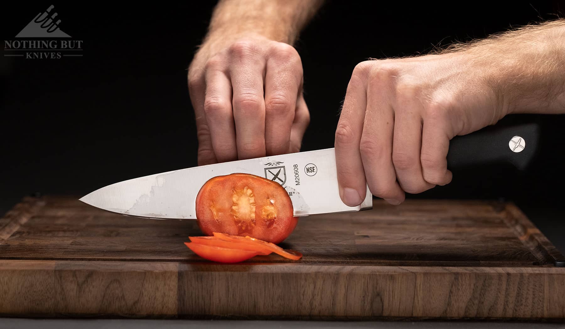 A close-up of a Mercer Genesis series chef knife slicing a tomato to show the high performance of the knives in this set. 