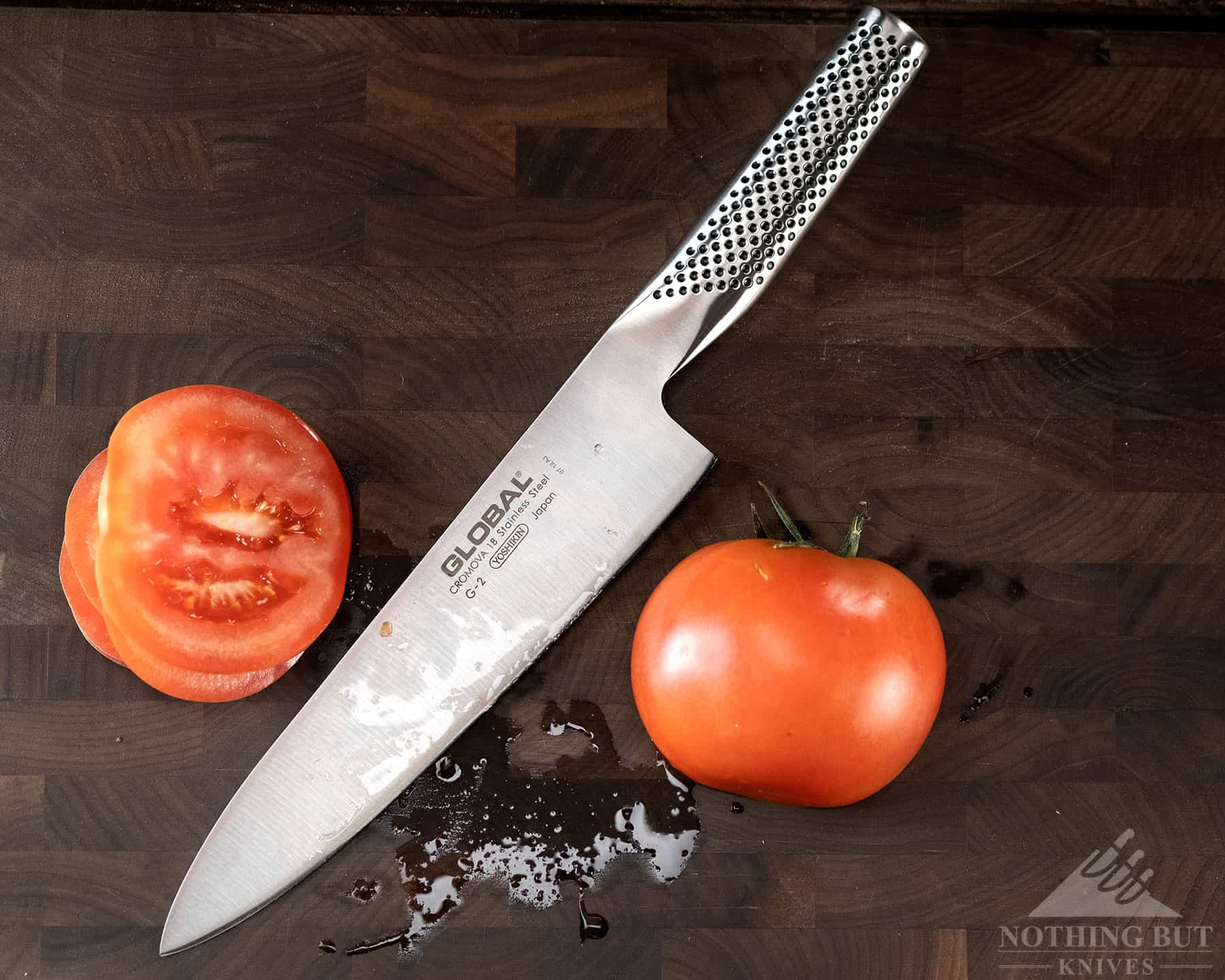 The Global G-2 chef knife shown on a cutting board with a tomato it cut in half. 