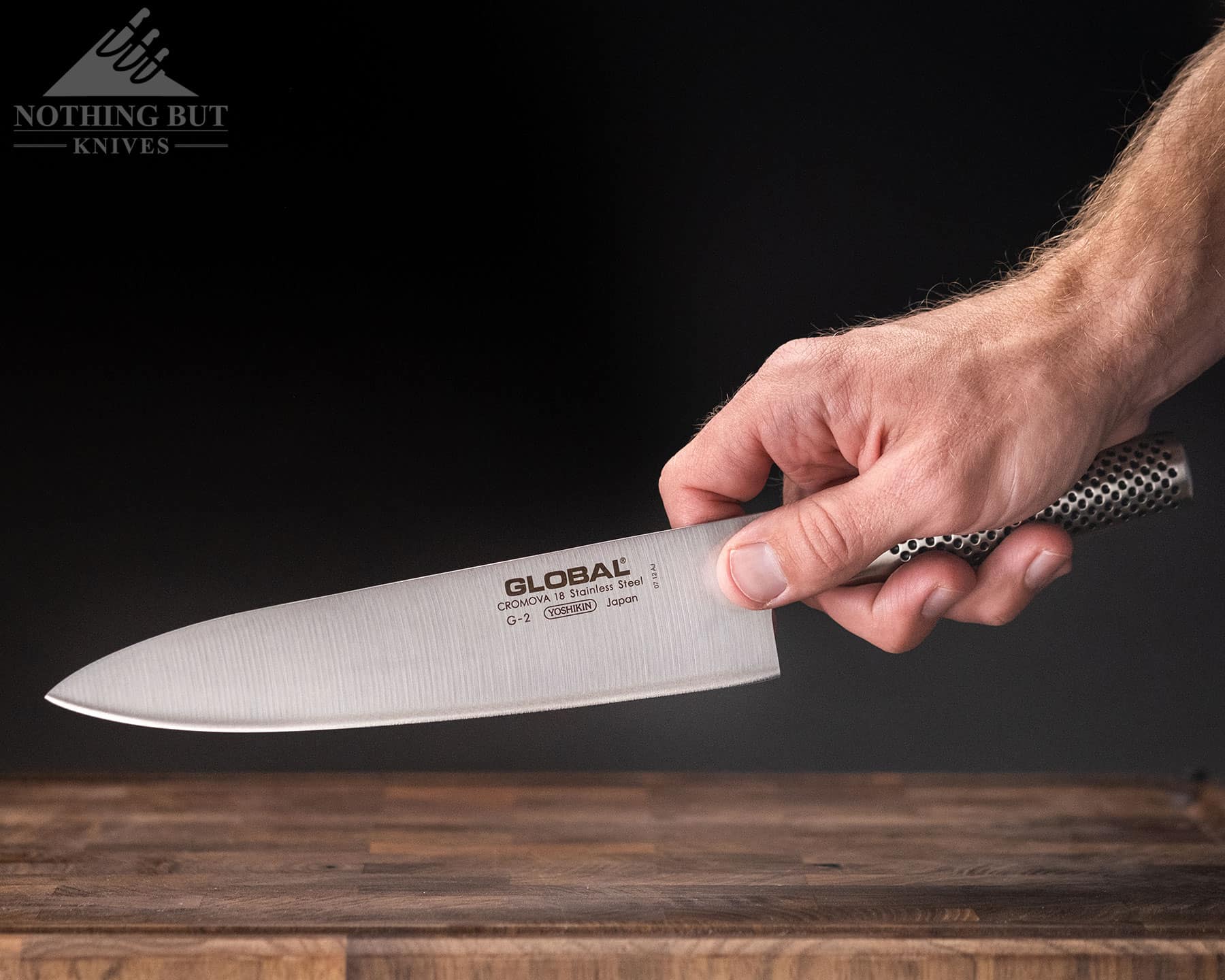 A close-up of a person's hand holding the Global G-2 chef knife in a pich grig to illustrate the handle ergonomics. 