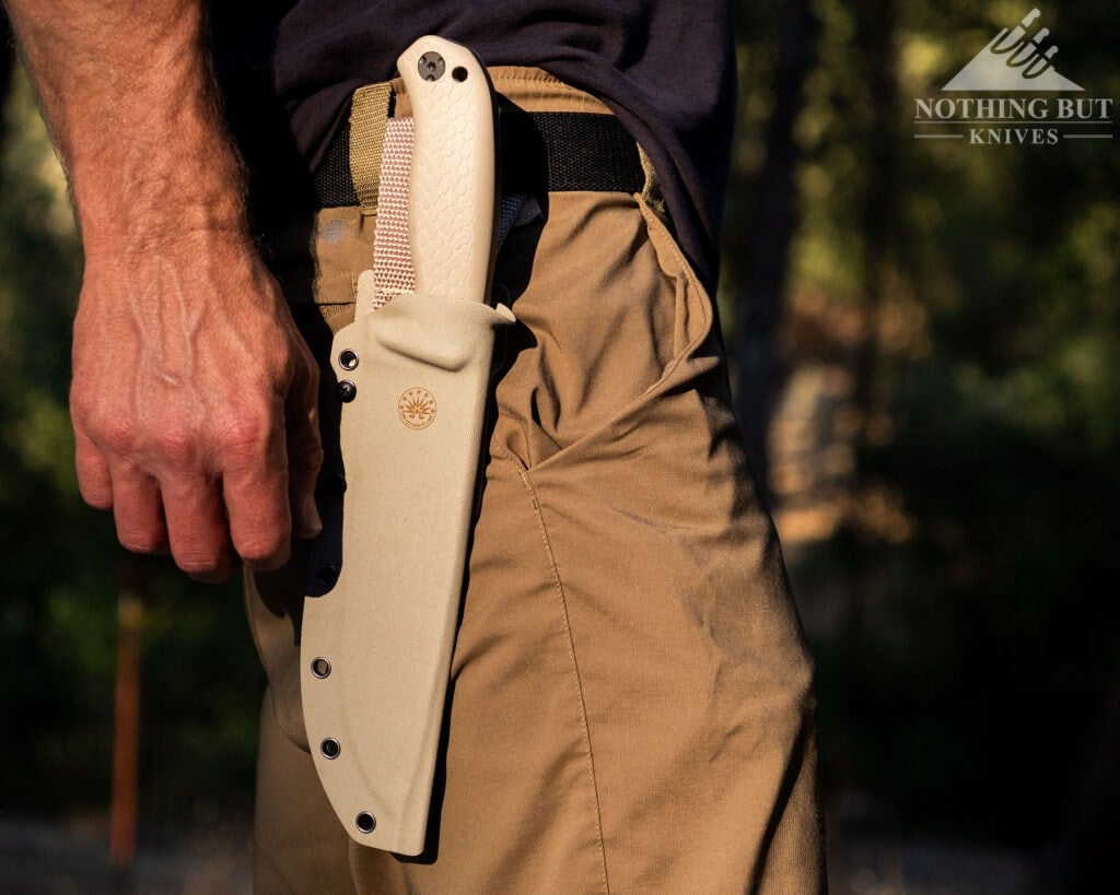 Top Survival Knife Beatdown - Hands On Testing - Image 11 The Coyote version of the Off-Grid Tracker XXL in its sheath on a person's hip in a forest.