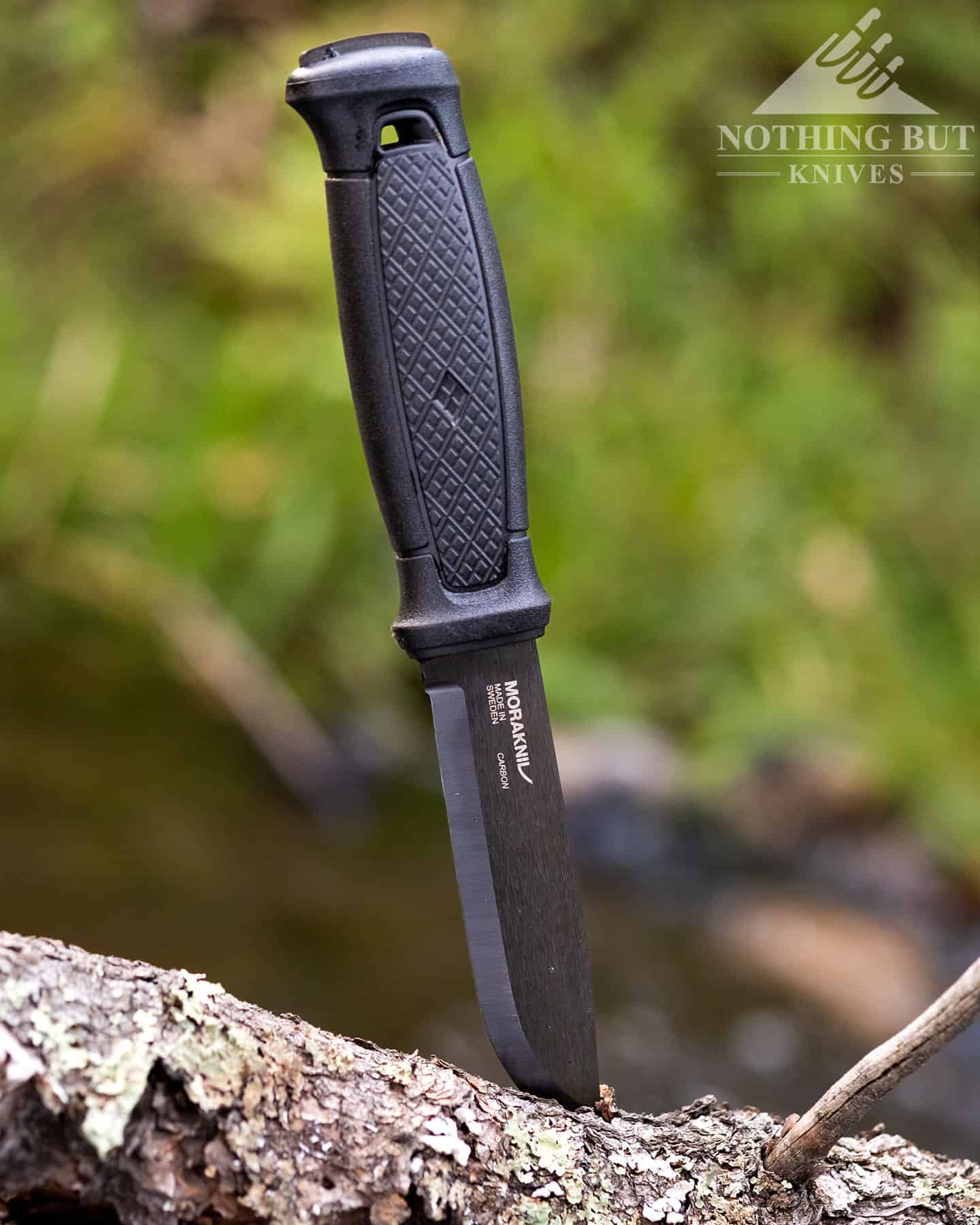 The Morakniv Garberg full tang bushcraft knife with its blade tip stuck in a log in the forest.