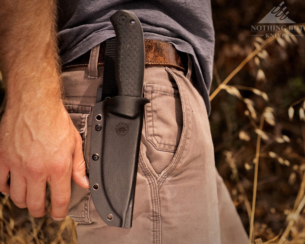 A close-up of the Off-Grid Tracker-X3 fixed blade in its kydex attached to a brown. leather belt on a person's waist.