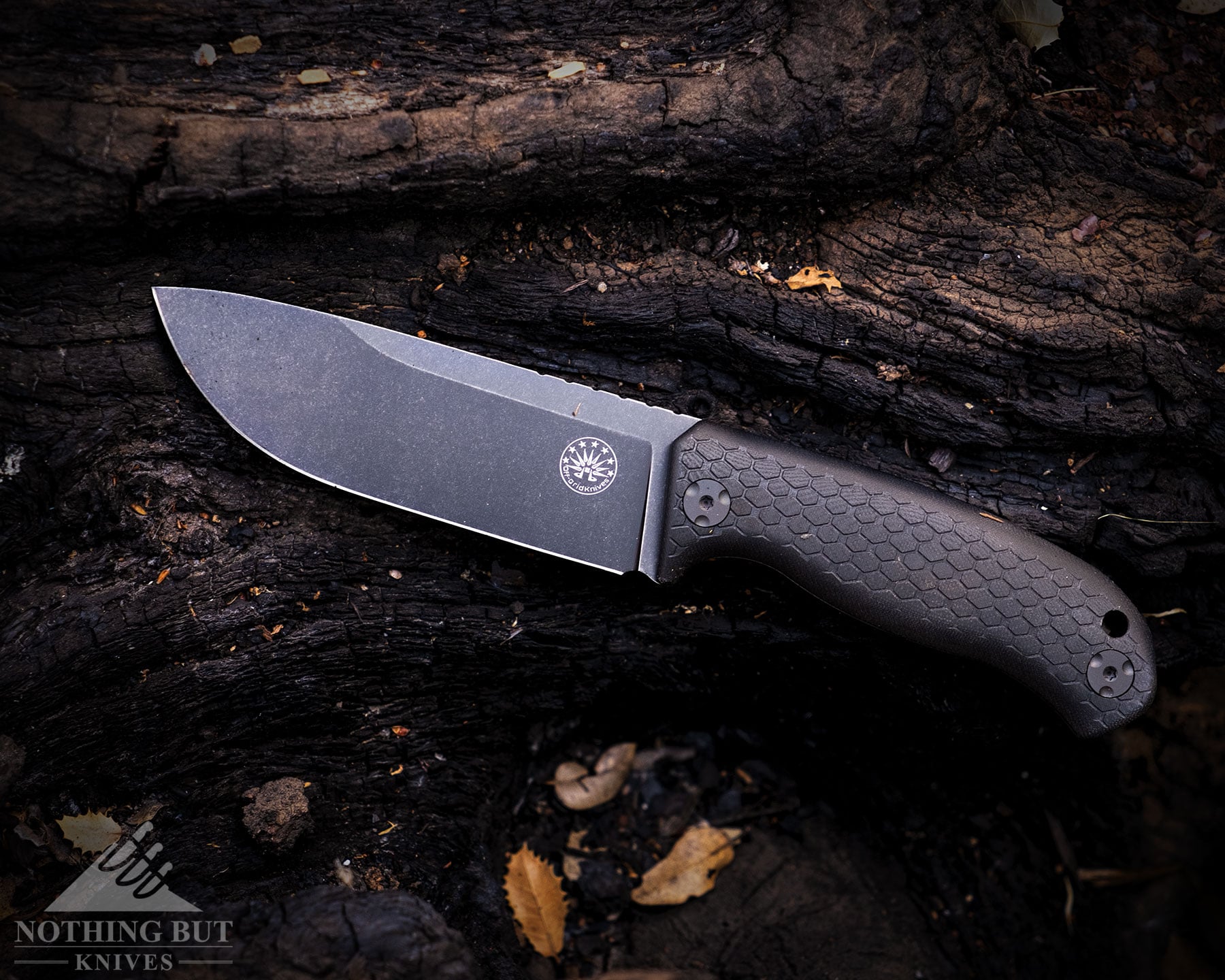 An overhead view of the Off-Grid Tracker-X3 bushcraft knife on top of a log that has been burned in a forest fire. 