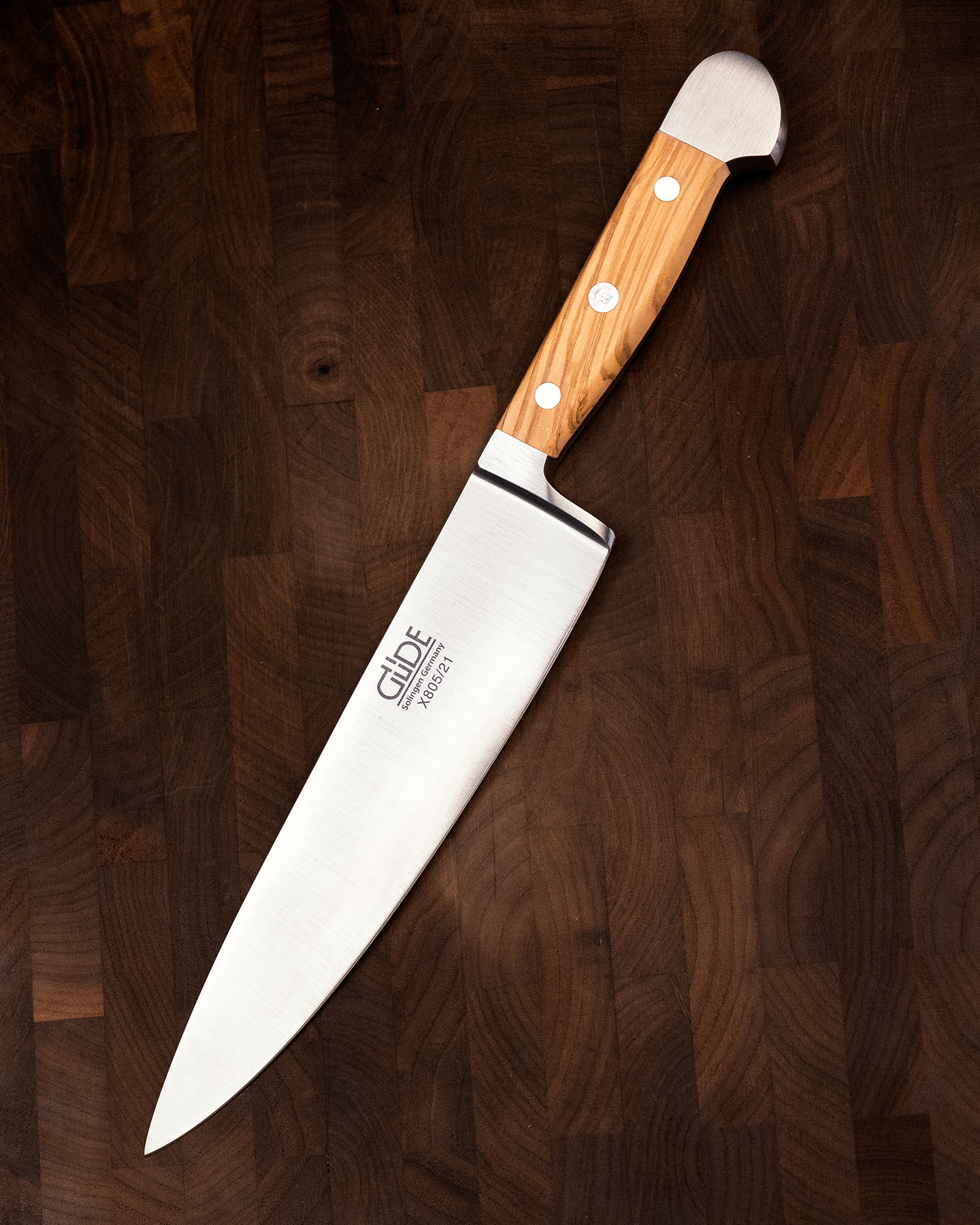 An overhead view of the Gude Alpha Olivewood handle chef knife on an end grain cutting board.