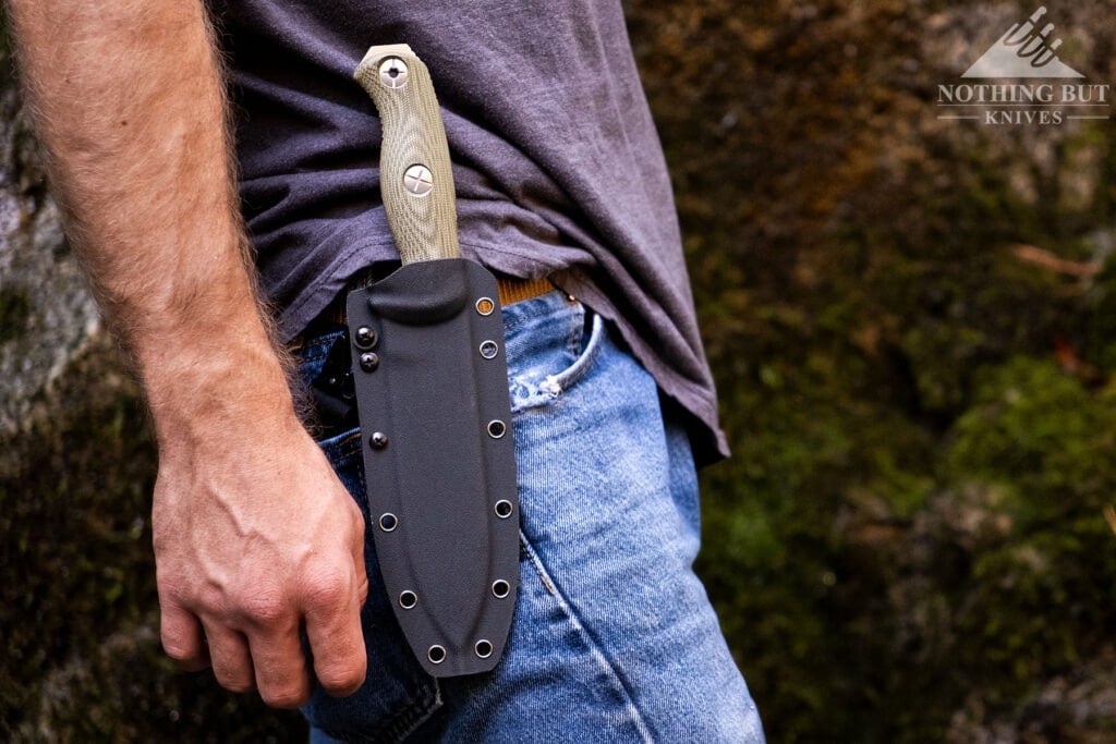Kizer Fixed Blade Knife Guide - Image 4 A side view of the Kizer Drop Bear fixed blade knife in its kydex sheath attached to a brown leather belt on a person's hip.