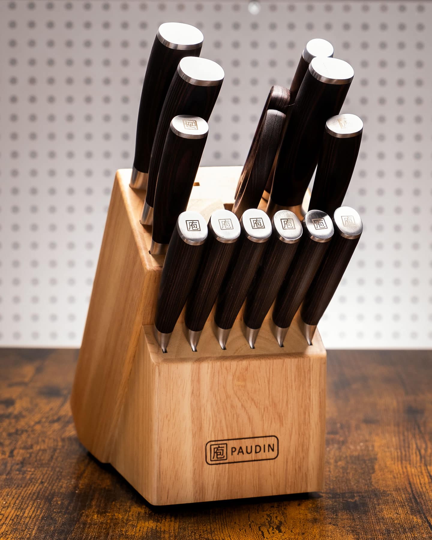 The Paudin 14-piece knife set shown here on a wood table in front an off-white background.