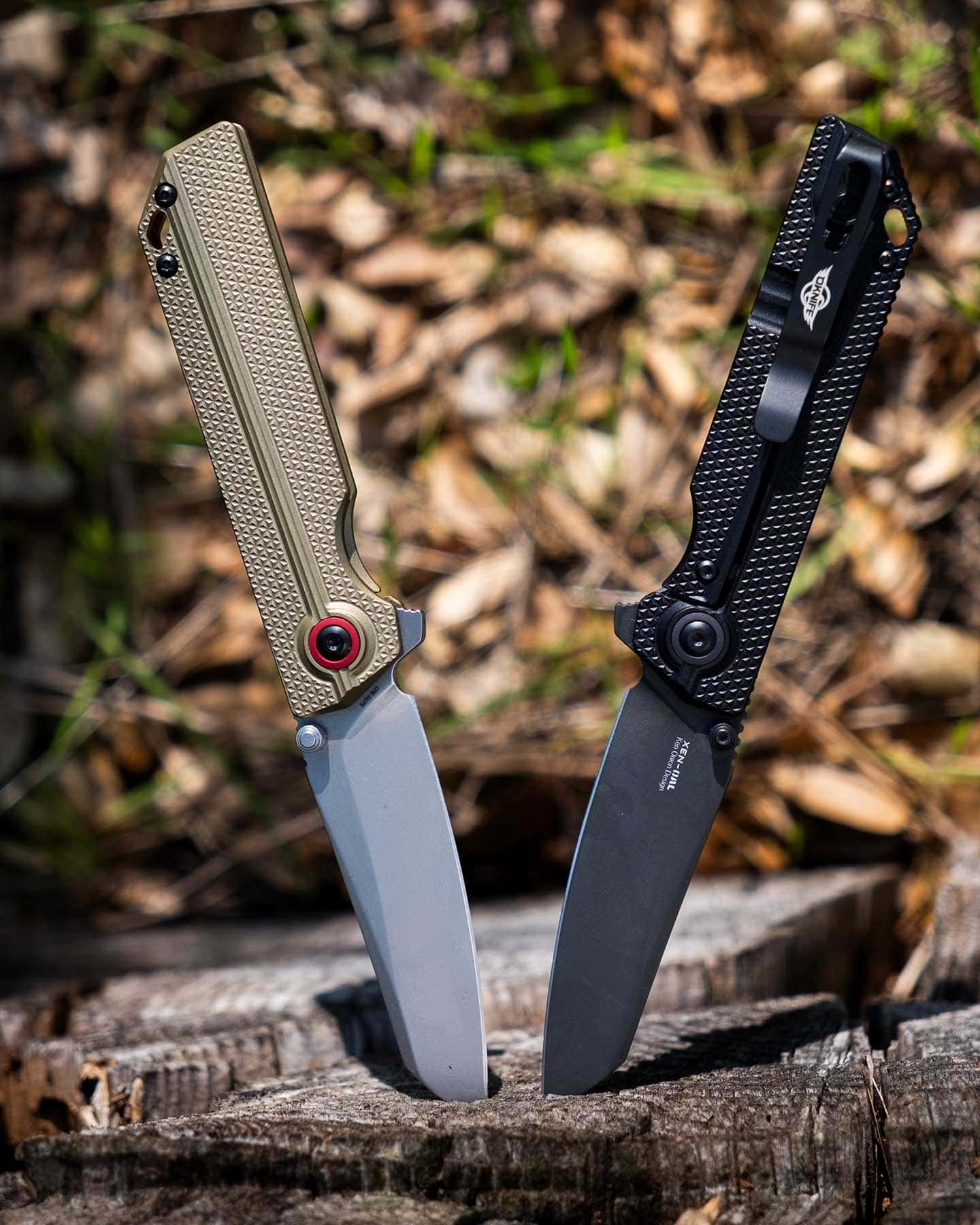 Both versions of the Oknife XEN-OAL pocket knife sticking out of a log outdoors.