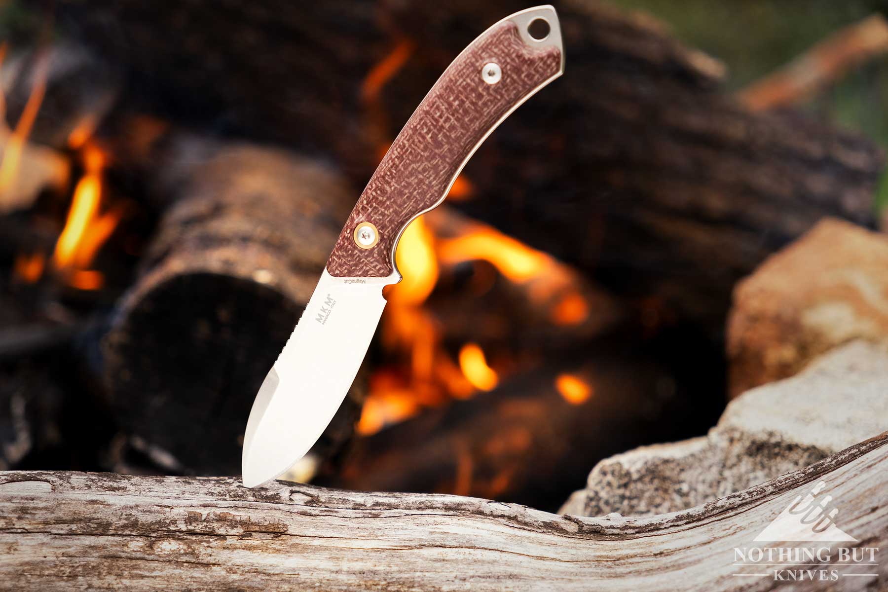 Off-Grid Sidekick Review - Image 9 The MKM Pocket Tango fixed blade EDC knife sticking out of a log next to a campfire in a forest in Northern California.