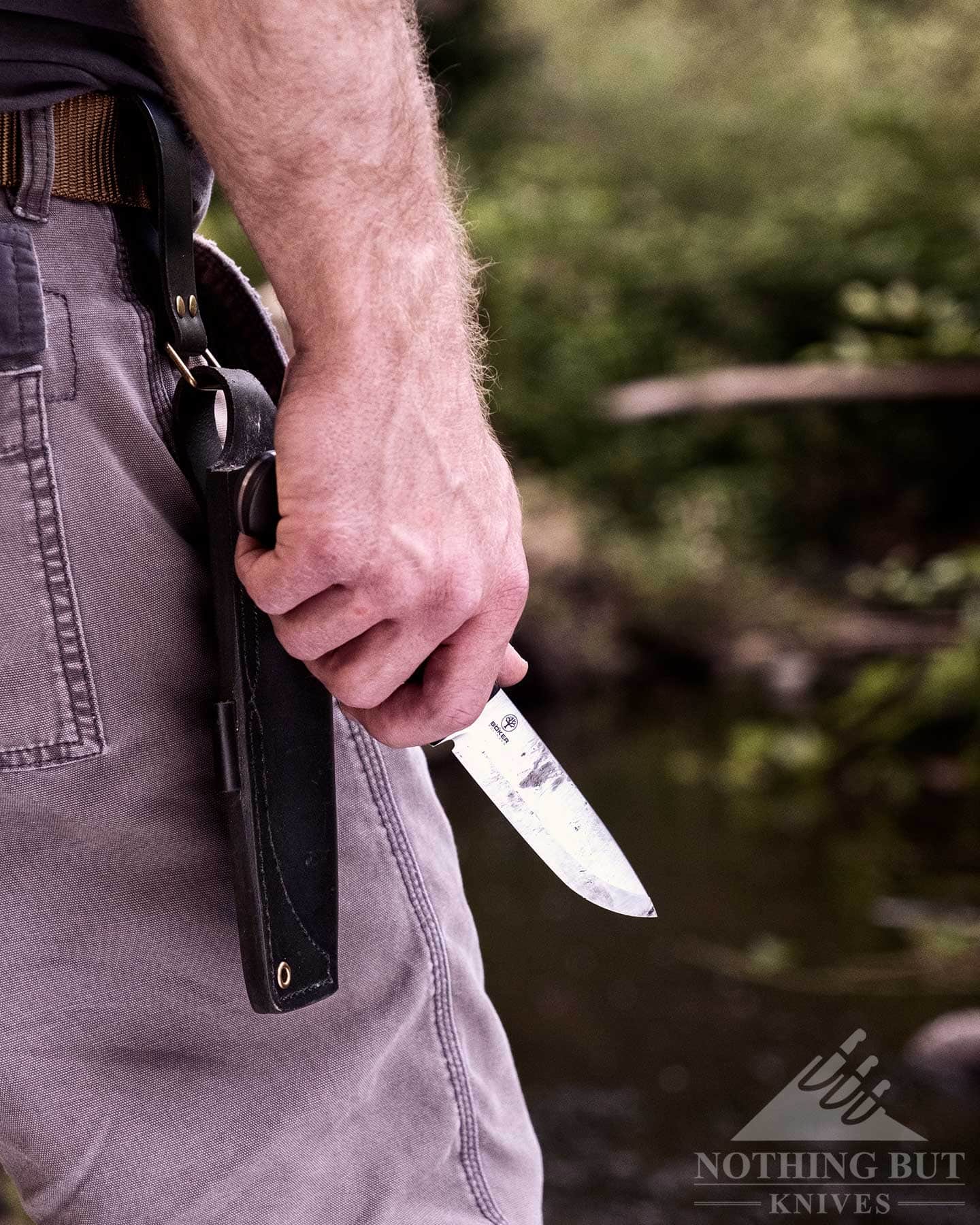 Boker Dbk Bushfriend 2000 Review - Image 15 A close-up of the Boker DBK Bushfriend 2000 in a person's hand at waist level in front of a mountain creek.