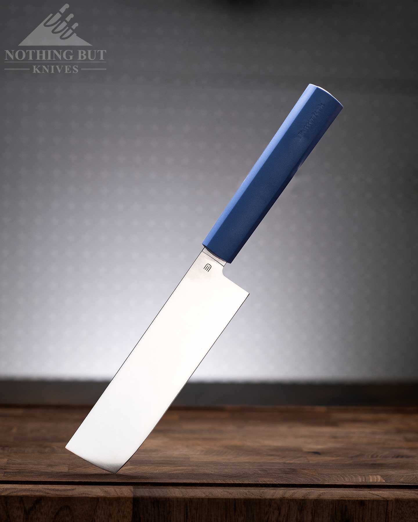 Review Of The Butterfork 4 Piece Kitchen Knife Set - Image 2 A blue handled Nakiri knife on a wood cutting board in front of an off-white background.