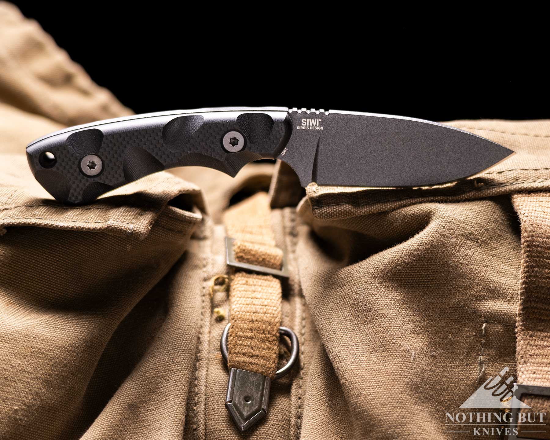 T.kell Wharnedc Review - Image 14 A black CRKT SIWI knife sitting on top of a military backpack in front of a black background.