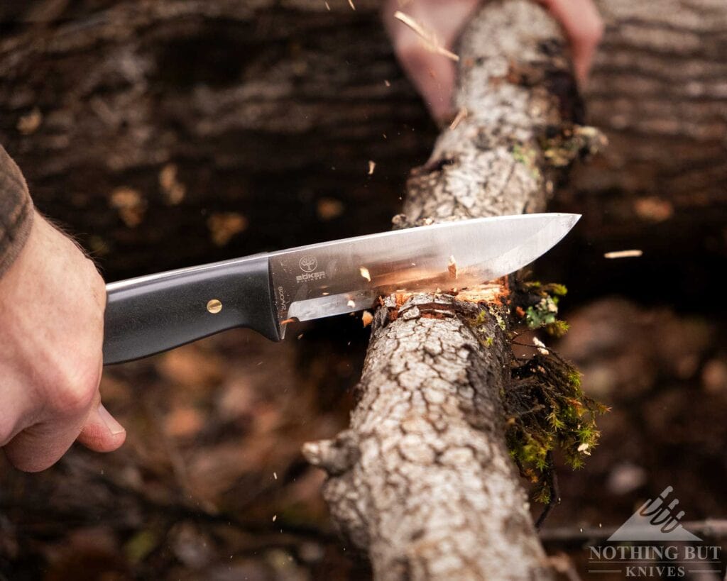 Boker Dbk Bushfriend 2000 Review - Image 12 A close-up of a bushcraft knife being used to chop through a small log on the ground in a forest.