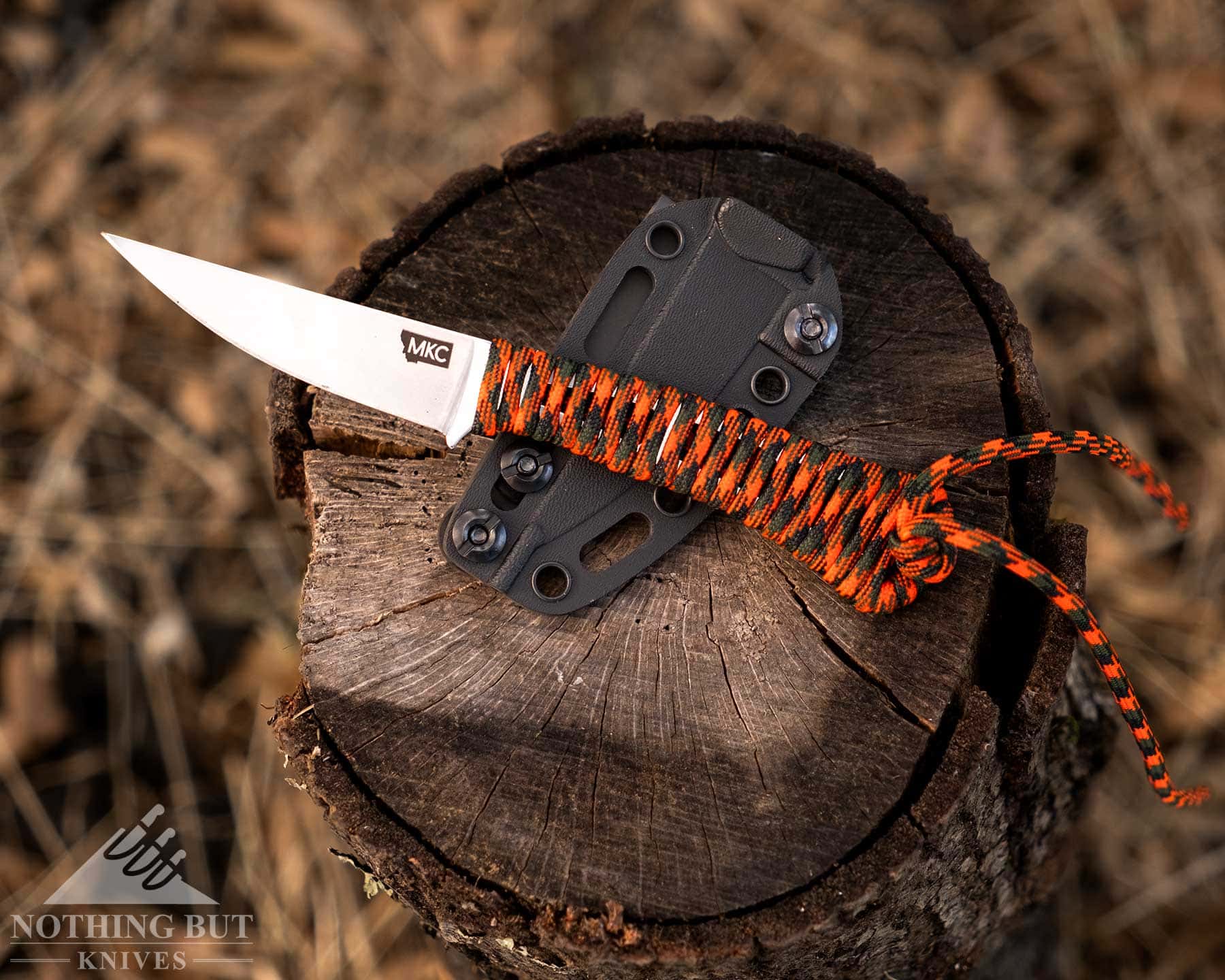Our Favorite Fixed Blade Edc Knives And How To Carry Them - Image 28 An overhead view of the MKC Speedgoat 2.0 fixed blade knife sitting on its kydex sheath on top of a piece of firewood in a field of brown grass.