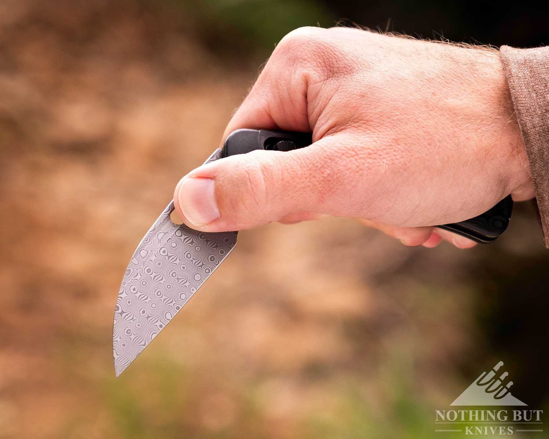 Kansept Vivid Review - Image 4 A close-up of a person'e right hand opening the blade on a Kansept Vivid folding knife using the thumb hole.