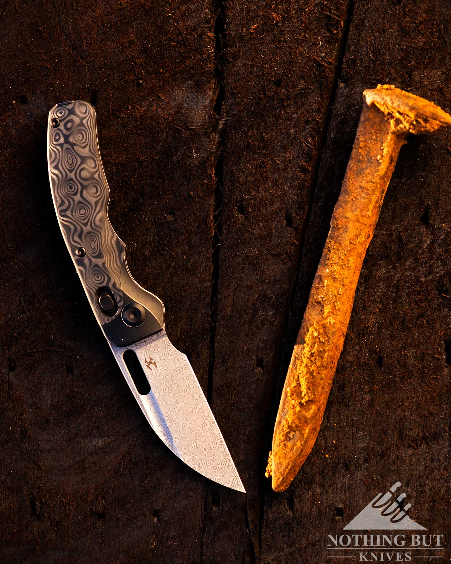 Kansept Vivid Review - Image 1 An overhead view Kansept Vivid folding knife with its blade in the open position next to a railroad spike to show scale.