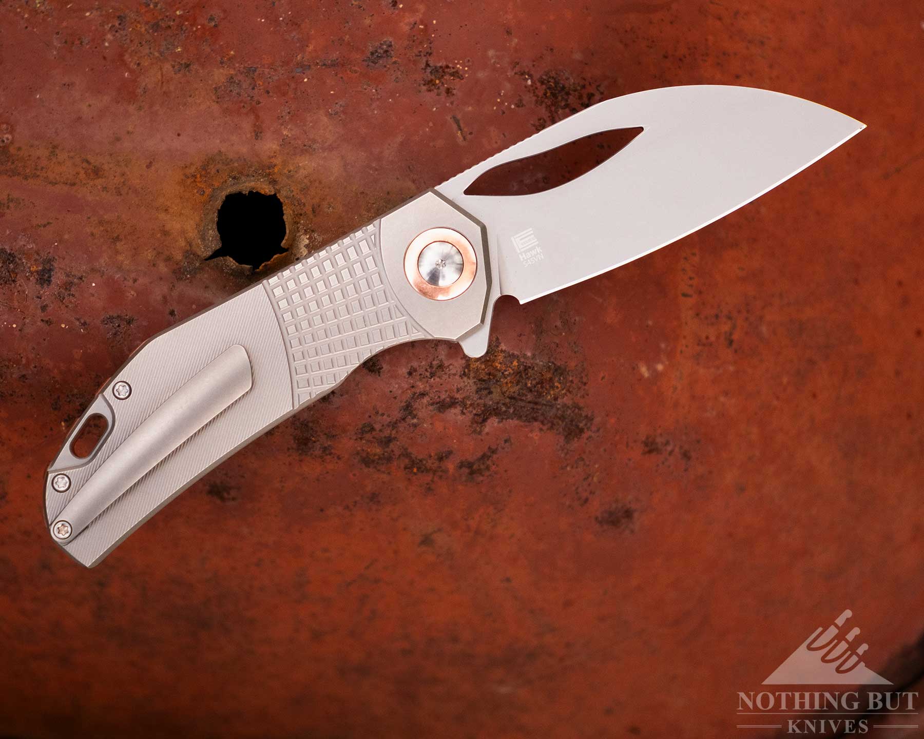 Kansept Vivid Review - Image 8 An overhead view of the Kizer Hawk pocketknife with its blade in the open position on a rusty, metal background.