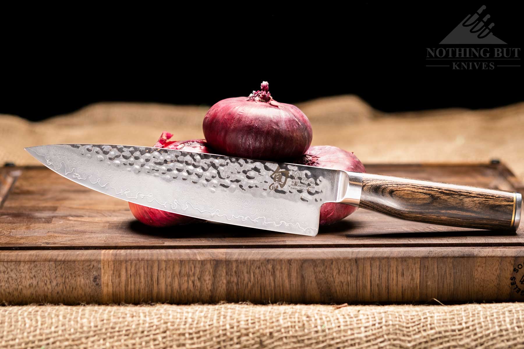 Demko Gyuto Chef Knife Review - Image 7 A Shun Premier chef knife on a dark wood cutting board with three small red onions in front of a black background.