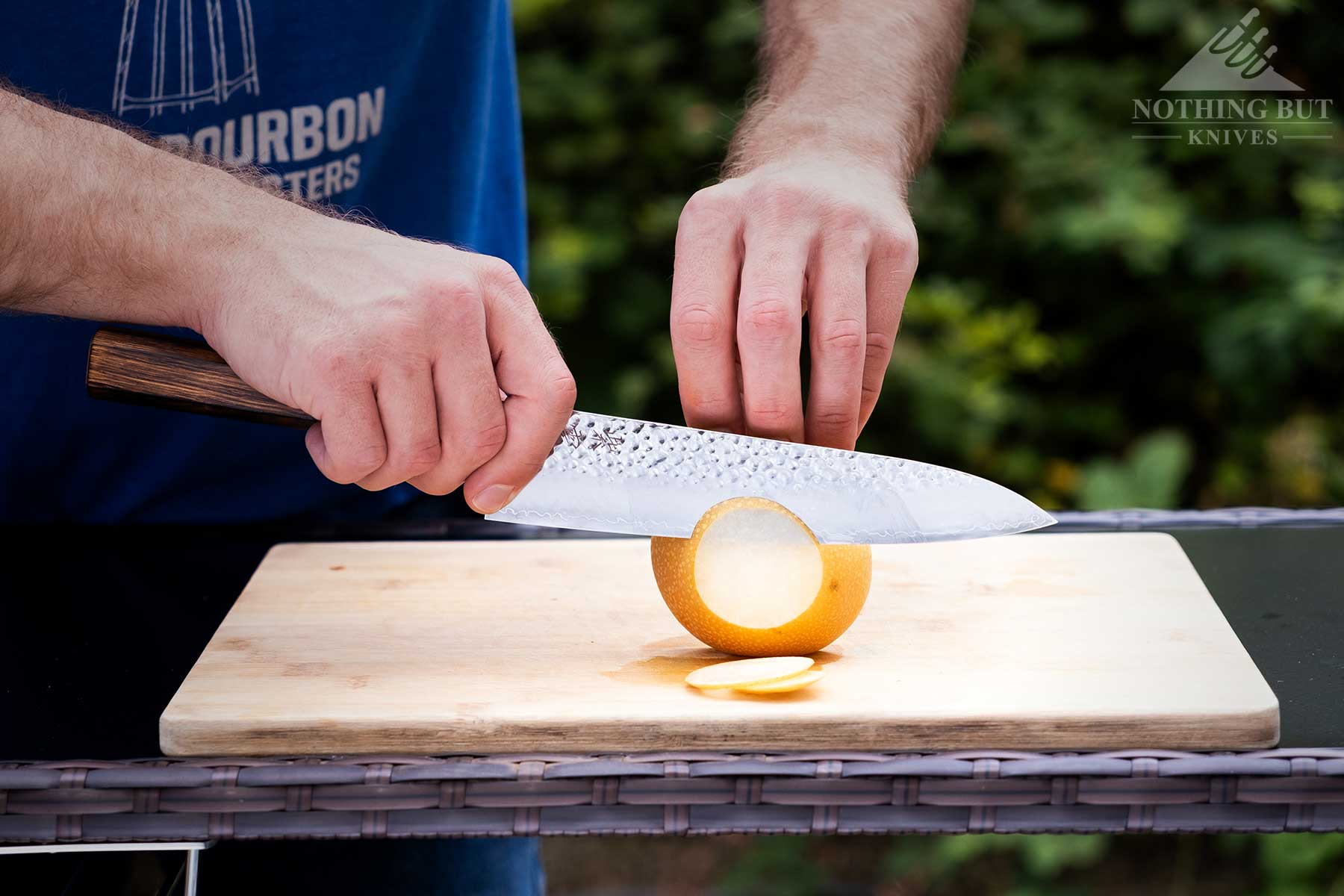 Demko Gyuto Chef Knife Review - Image 3 A close-up of the Demko Knives Gyuto chef knife being used to slice an Asian pear outdoors on a bamboo cutting board.