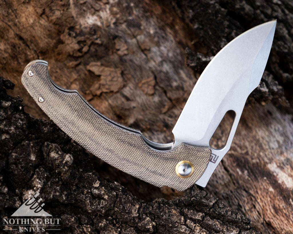 The Green Micarta handled version of the Artisan Xcellerator shown here with its blade in the half open position sitting on a large tree trunk. 