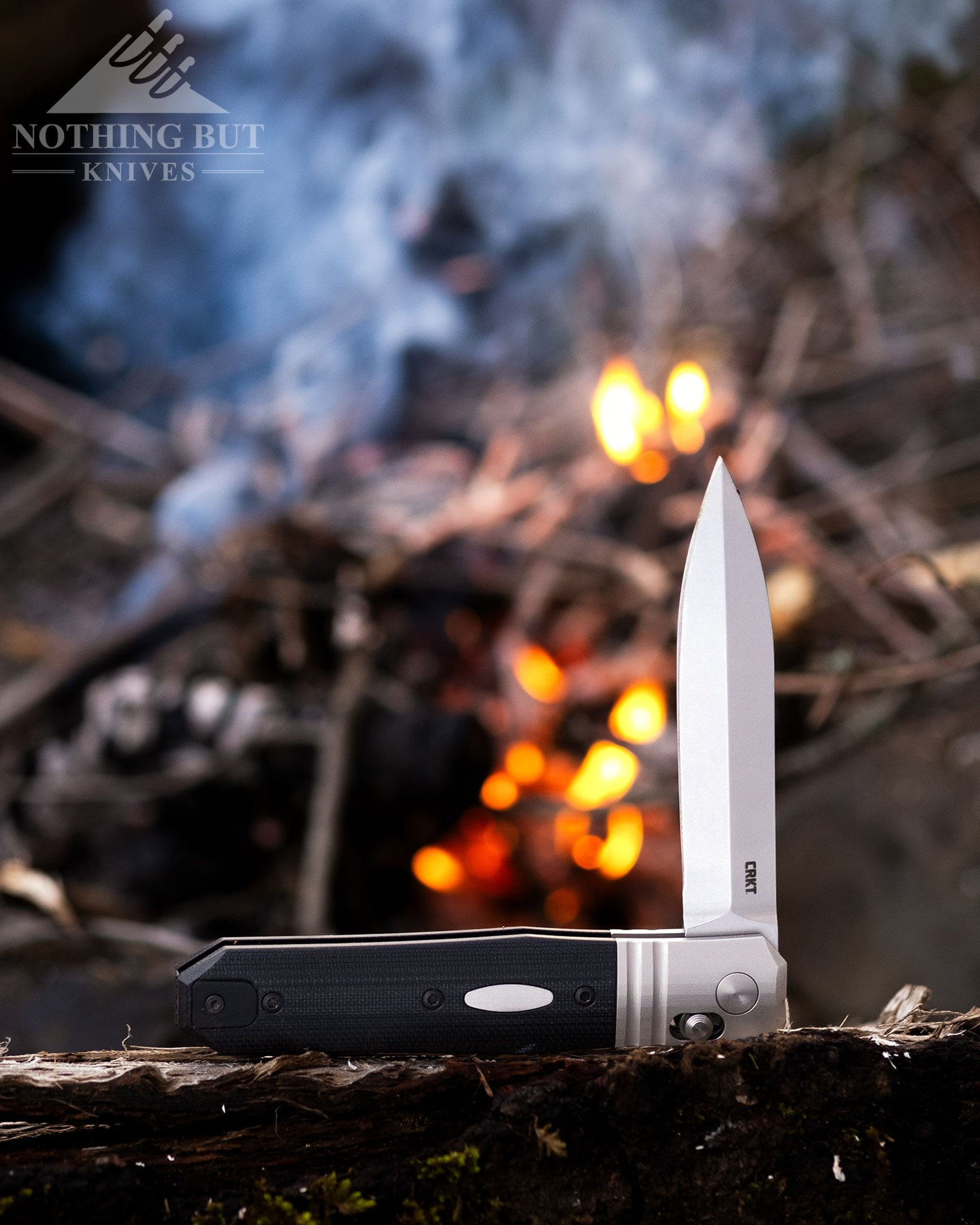 The CRKT Redemption folding knife shown here with its blade in the half open position in front of a campfire.