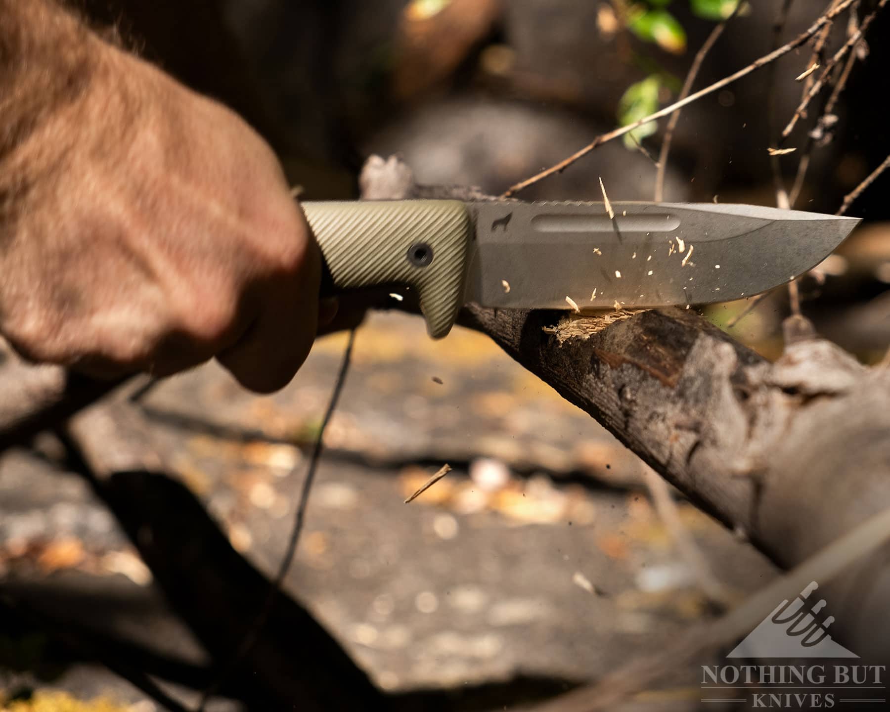 An action shot of the Reiff Vicon knife with G10 handle scales and a Magnacut blade being used to chop a tree branch. 