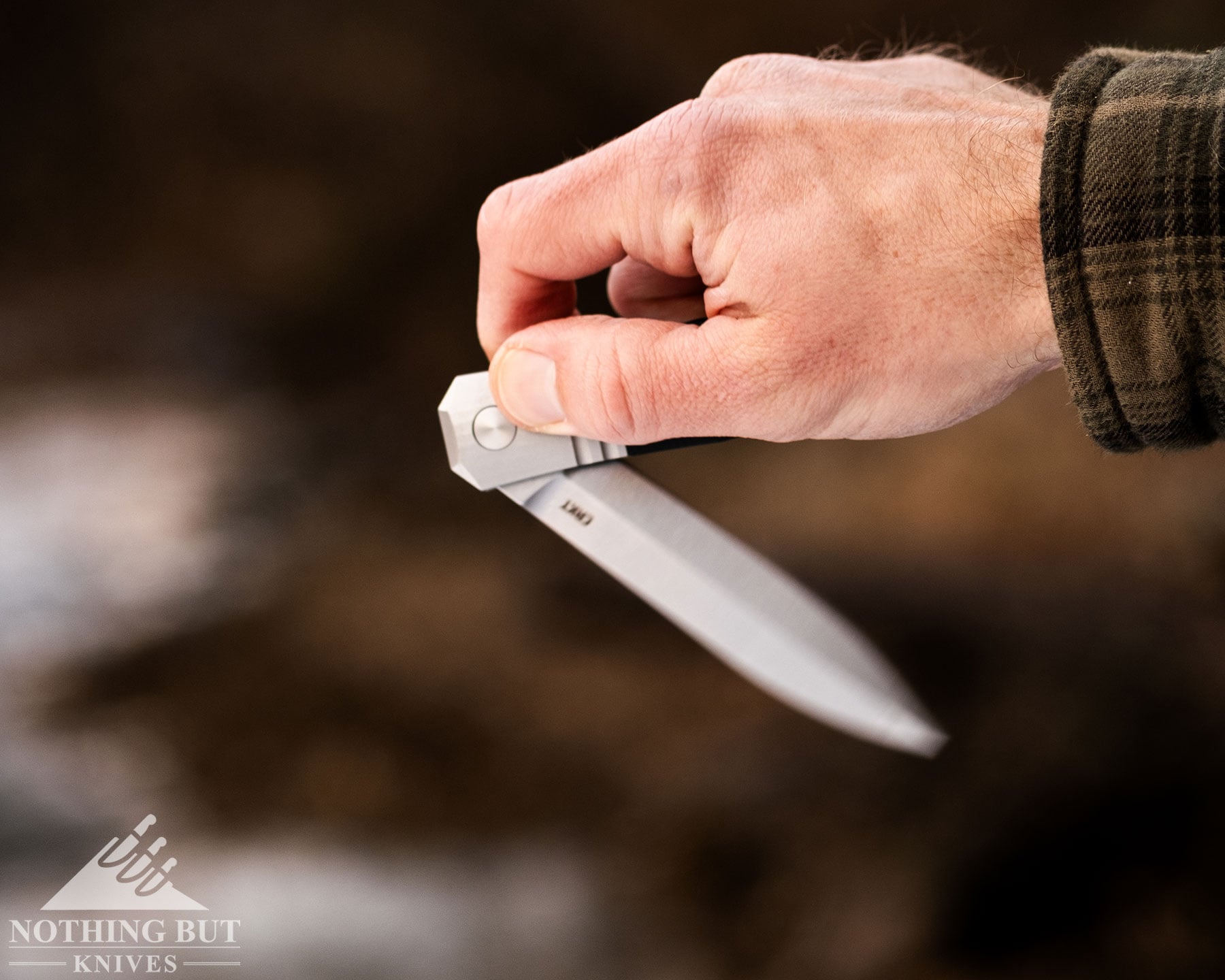 A close-up of a person's hand flipping open the CRKT Redemption folding knife outdoors to test its action. 