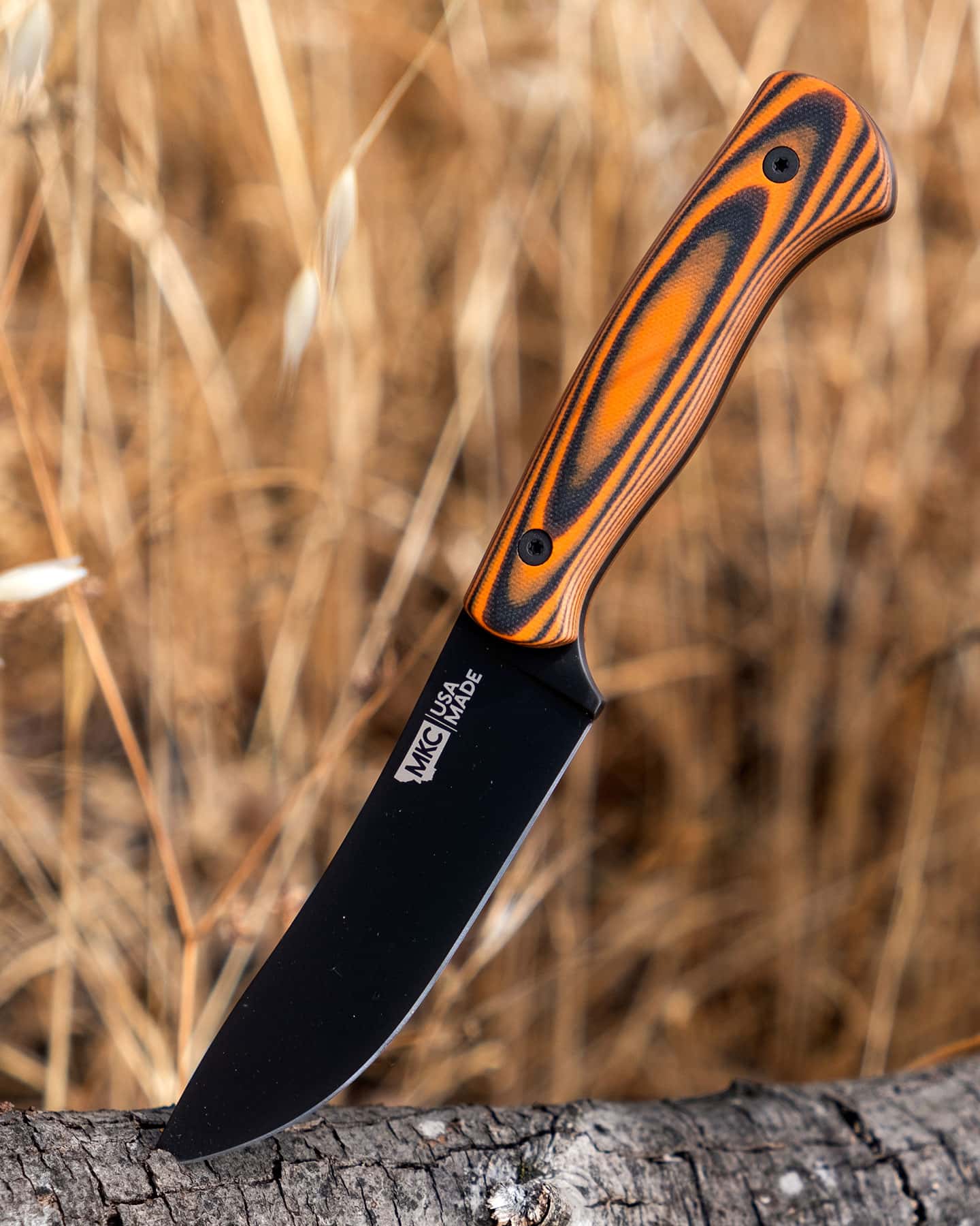 The Montana Knife Company Stonewall Skinner sticking out of a log in a field of brown grass.