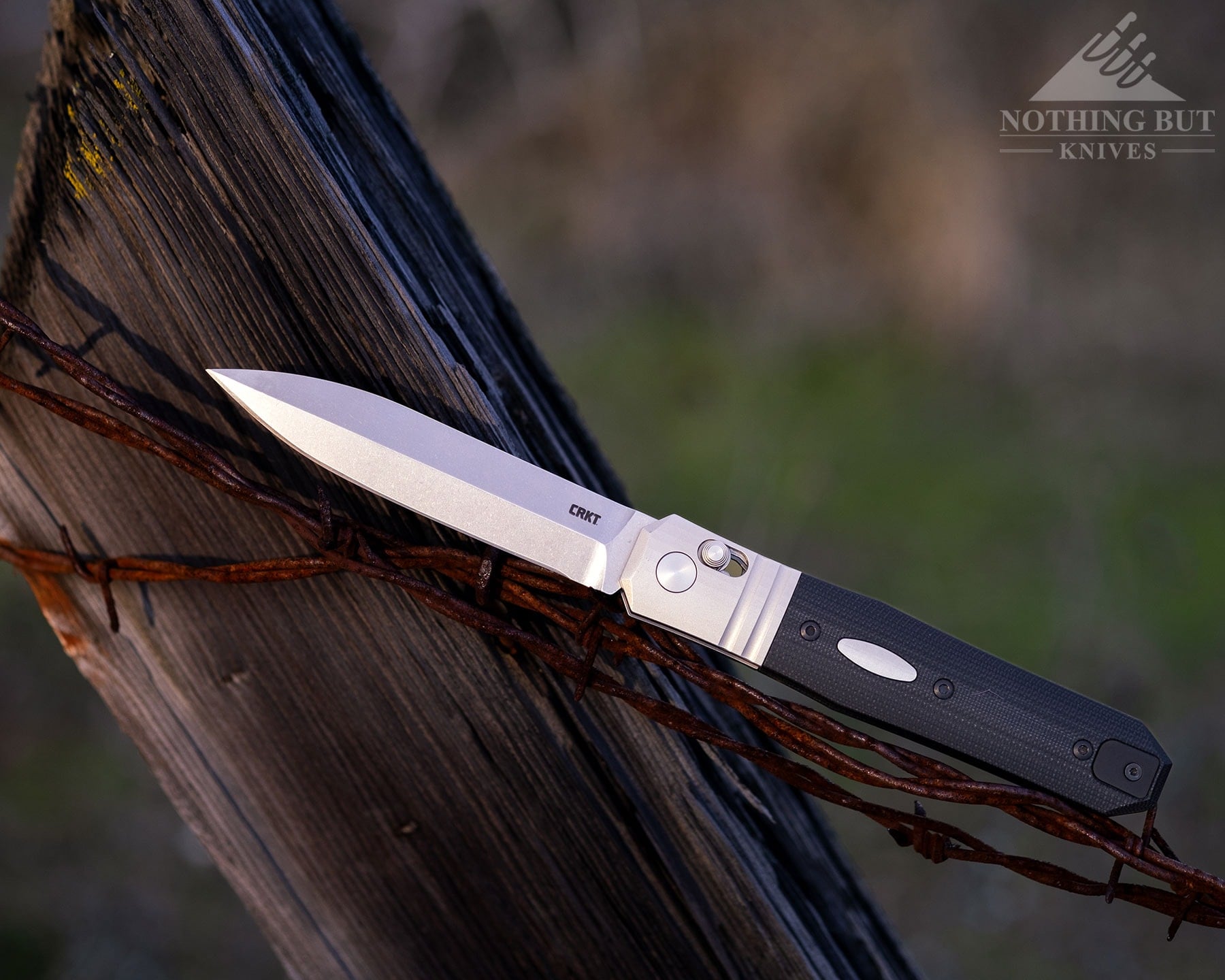 The CRKT Redemption with a Magnacut blade in the open position balanced on a barbed wire fence in a field.
