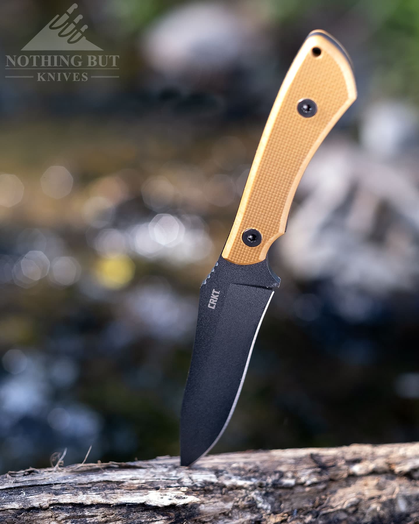 Toor Knives Brauler Review - Image 15 The CRKT Ramadi sticking out of a piece of wood next to a creek.