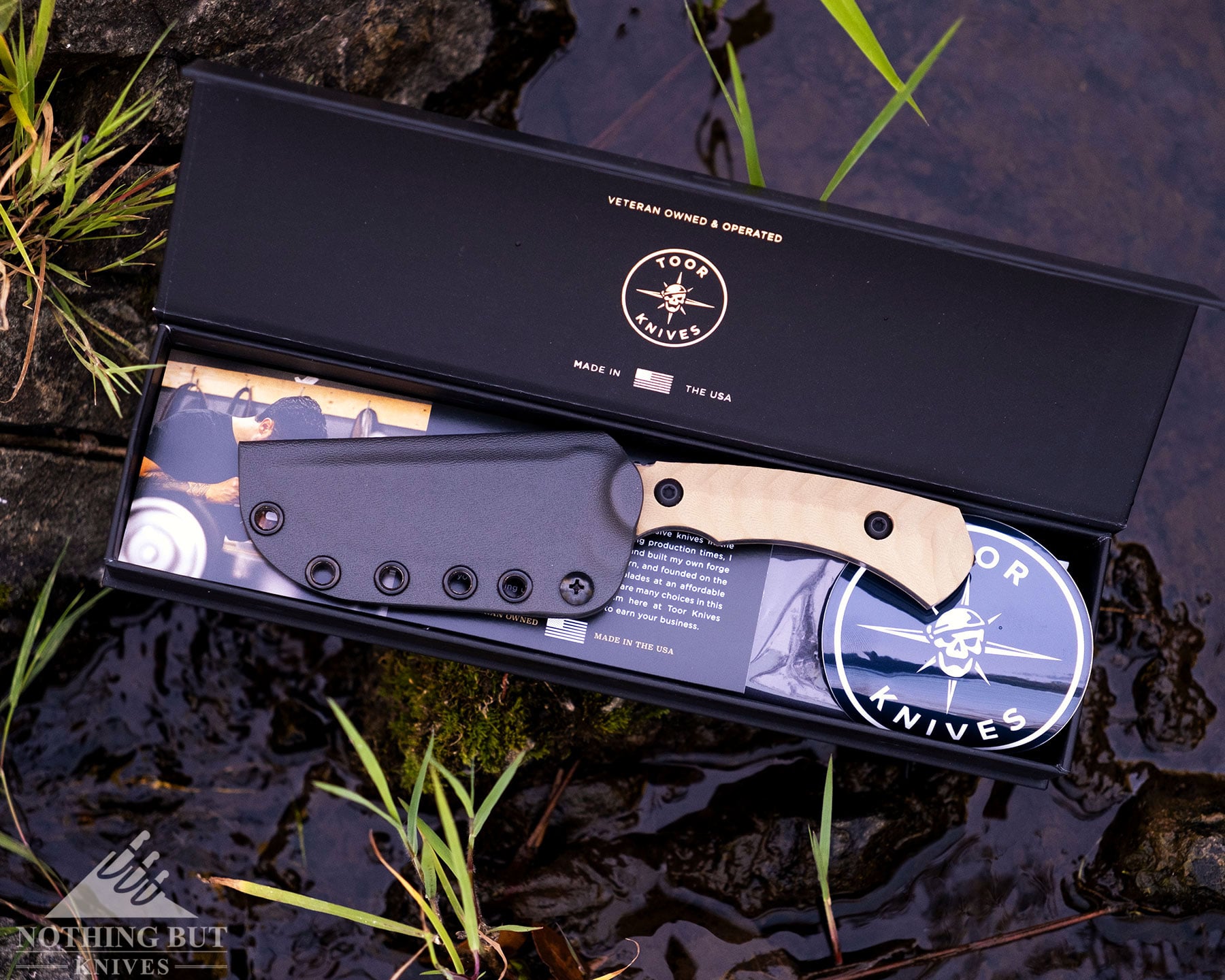 Toor Knives Brauler Review - Image 9 An overhead view of the Toor Brauler with its kydex sheath in its packaging on a rock in a small creek.