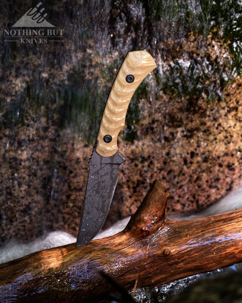 Toor Knives Brauler Review - Image 5 The Toor Brauler fixed blade sticking out of a piece of driftwood in front of a small waterfall in a mountain creek.