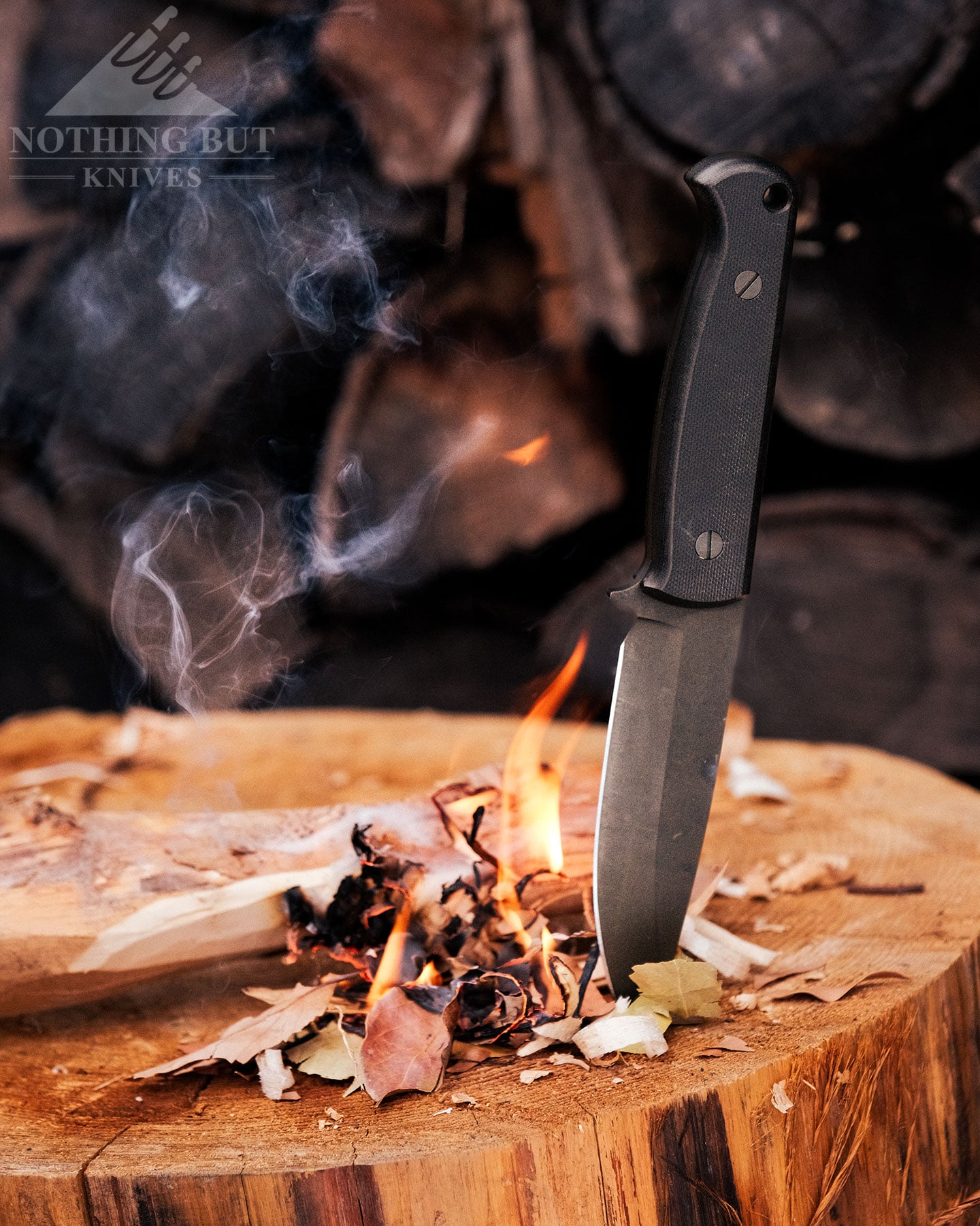 Skallywag Tactical. The Wanderer Review. - Image 12 The Skalleywag Wanderer bushcraft knife sticking out of a log next to a small fire it was used to start by scraping fire on a ferro rod.
