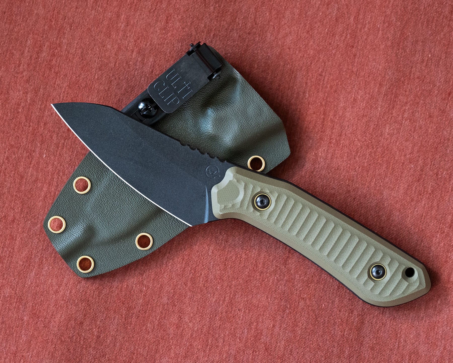 Blade Show West 2025 Wrap-Up - Image 17 The Schwarz Overland X fixed blade with its kydex sheath on a maroon background.