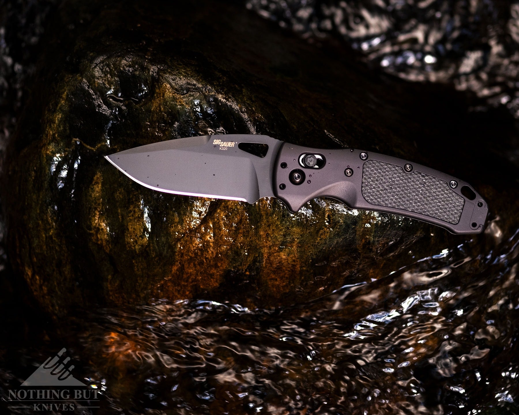 An overhead view of the Hogue-Sig-K320 pocket knife with its blade in the open position on a rock in a creek.  
