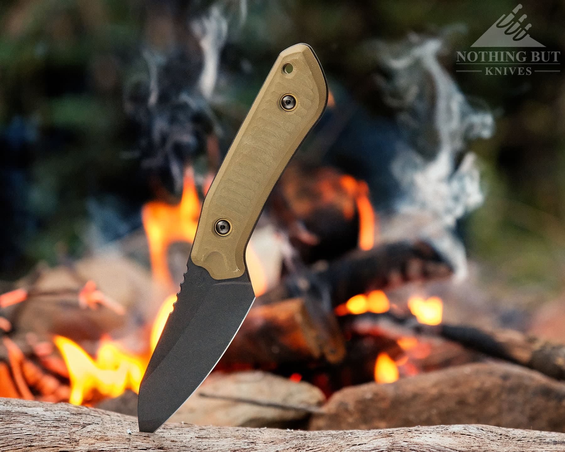 Schwarz Knives Overland X Review - Image 2 The Overland X fixed blade on a log next to a campfire in on the edge of the woods.