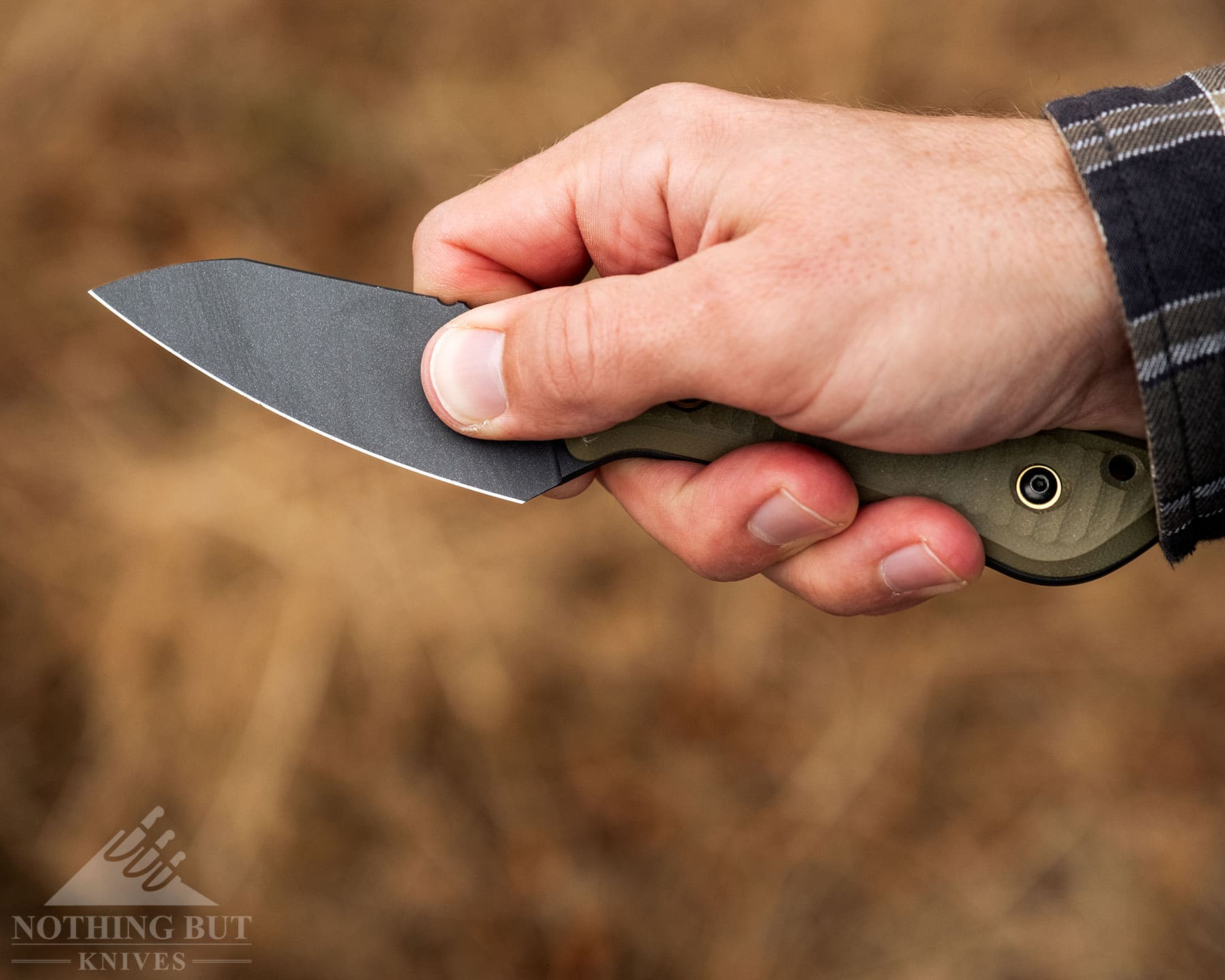 Schwarz Knives Overland X Review - Image 6 An overhead view of the Schwarz Knives Overland X being held in a pinch grip above a blurry, brown background.