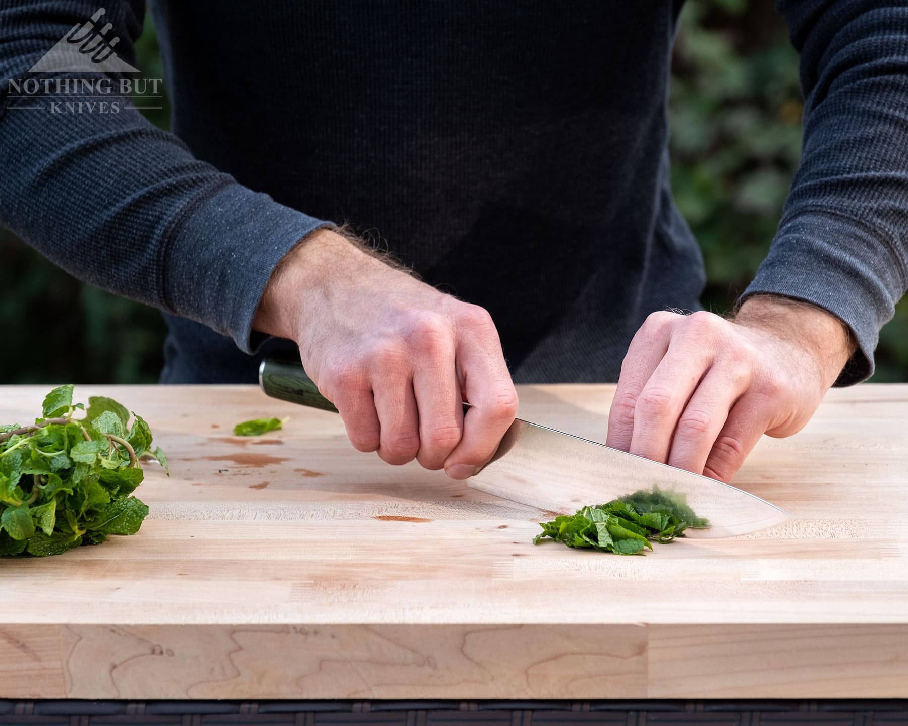 Hexclad Chef Knife Review - Is It Just Marketing Hype? - Image 6 A slightly elevated photo of the HexClad chef knife being used to chop mint leaves on a wood cutting board.
