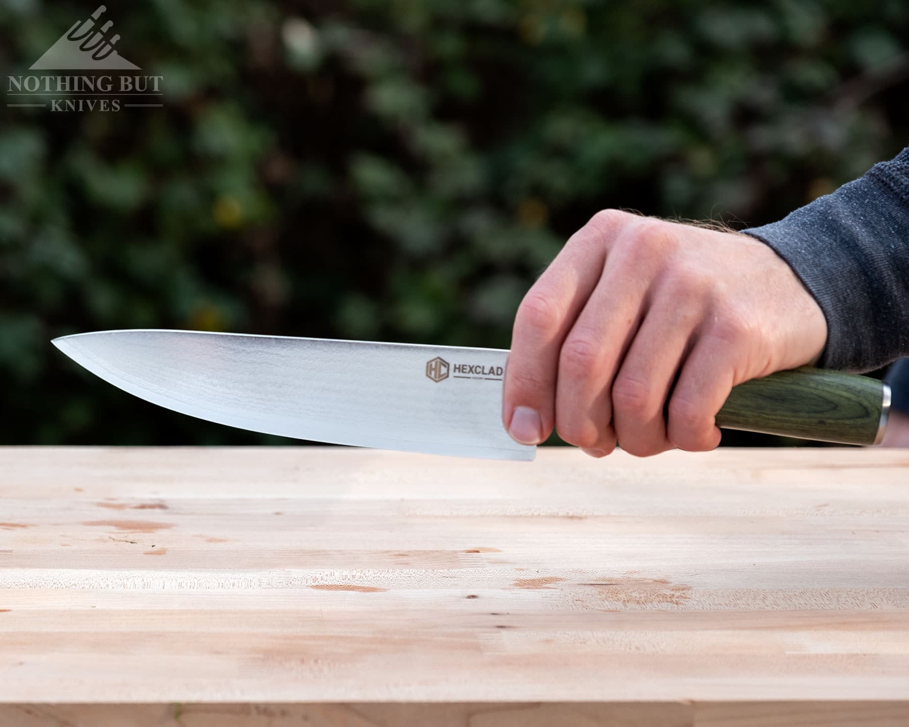 Hexclad Chef Knife Review - Is It Just Marketing Hype? - Image 3 A close-up of the HexClad 8-inch chef knife being gripped in a person's left hand above a wood cutting board.