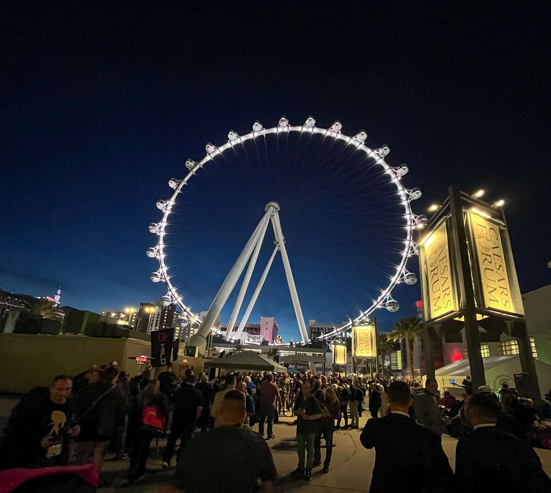 An evening image from the outdoor section of the Ceases Forum in Las Vegas during SHOT Show 2026 with people socializing in front of the Ferris wheel. 