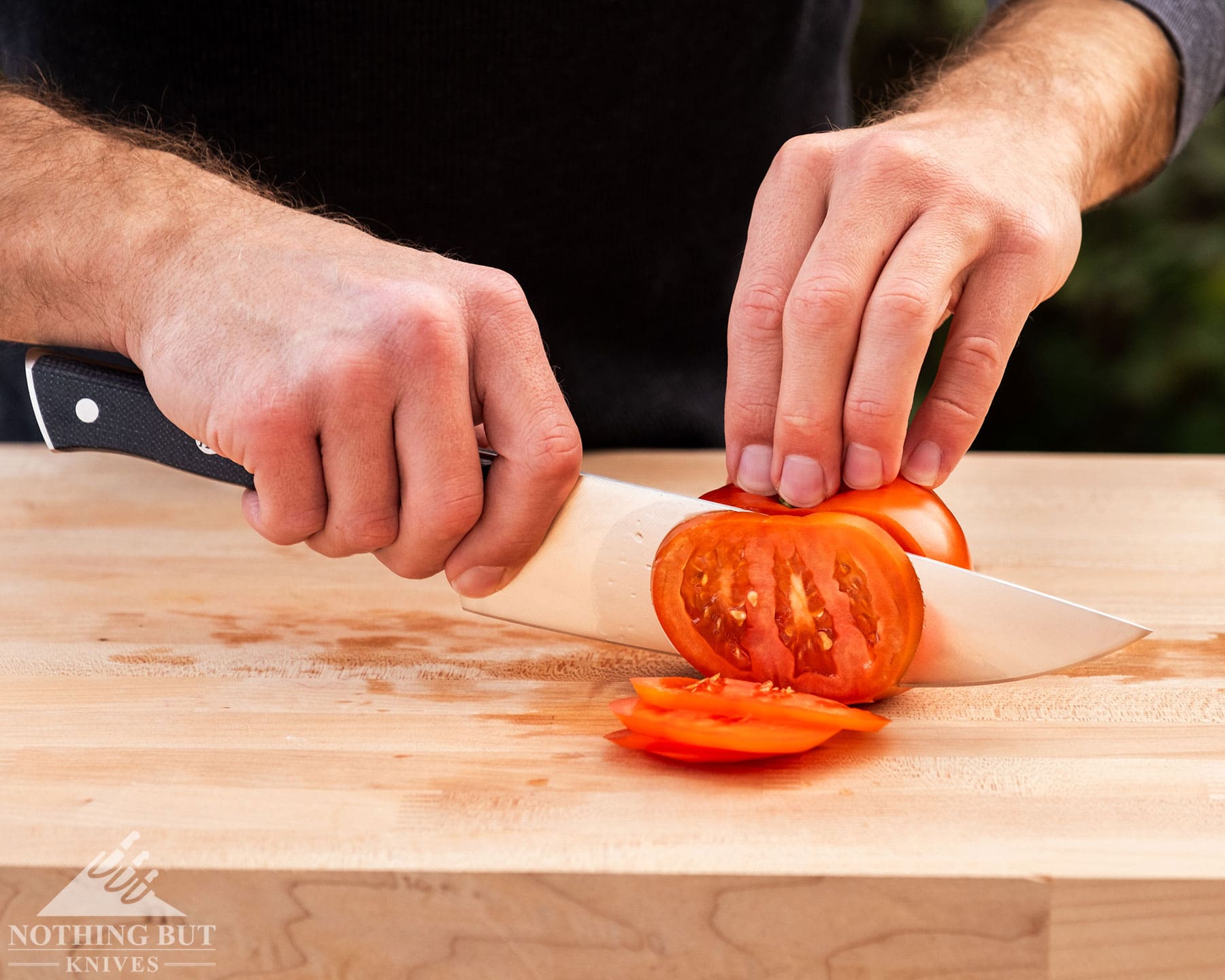 Zwilling Spectrum Chef'S Knife Review - Image 4 Zwilling Chef knife held in the right hand cutting a tomato on a wooden cutting board.