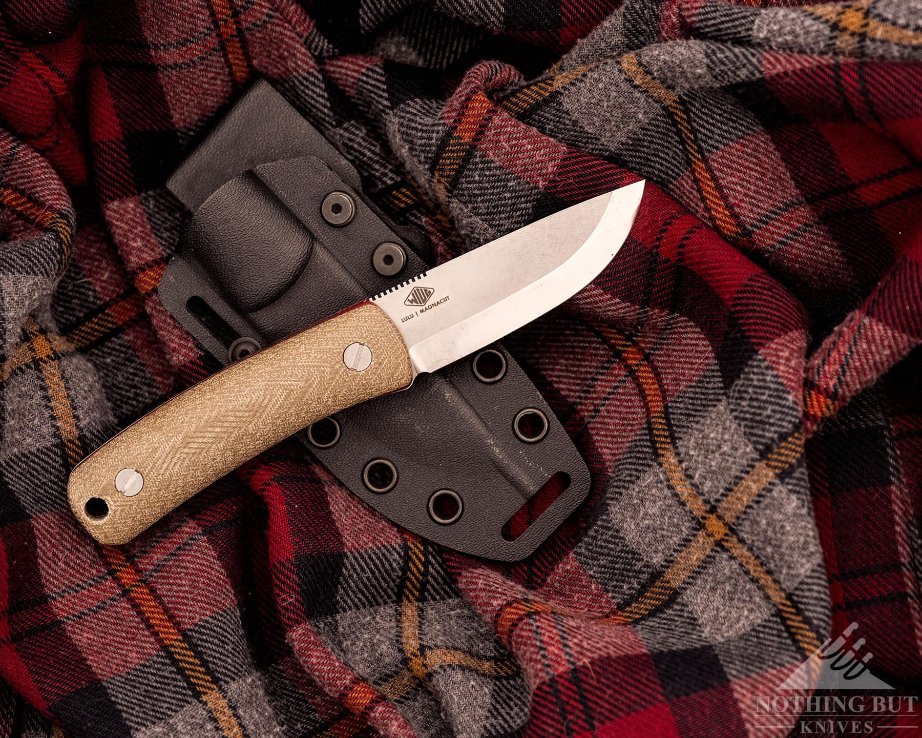 Knafs Lulu Review - Image 8 A fixed blade bushcraft knife lying on its side, on top of a sheath and flannel jacket.
