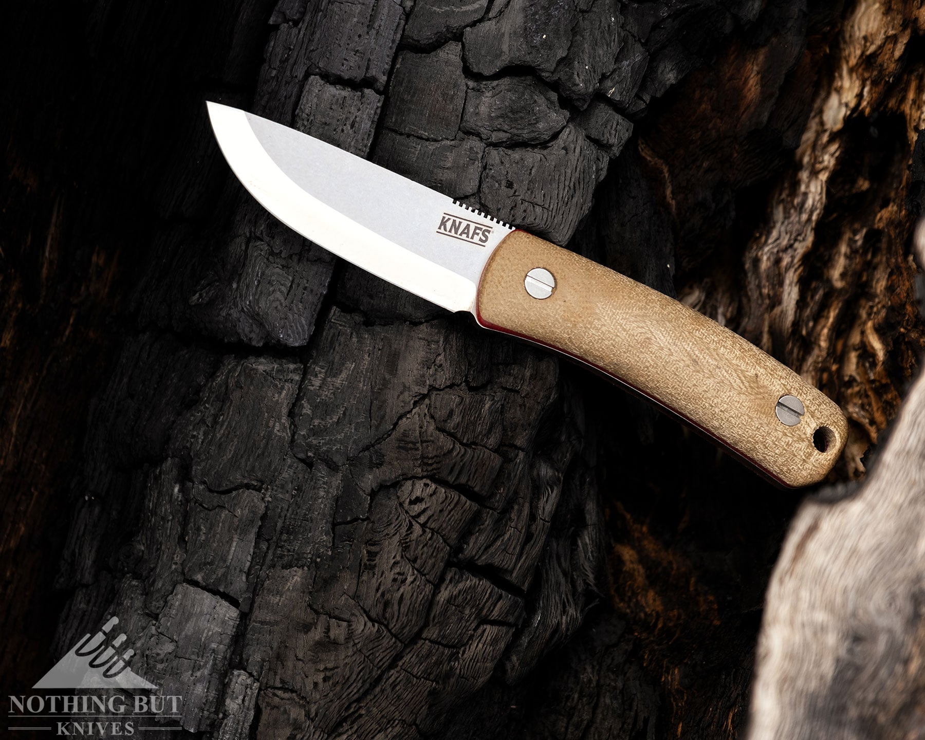 Knafs Lulu Review - Image 7 A bushcraft knife laying on its side on a burnt tree.
