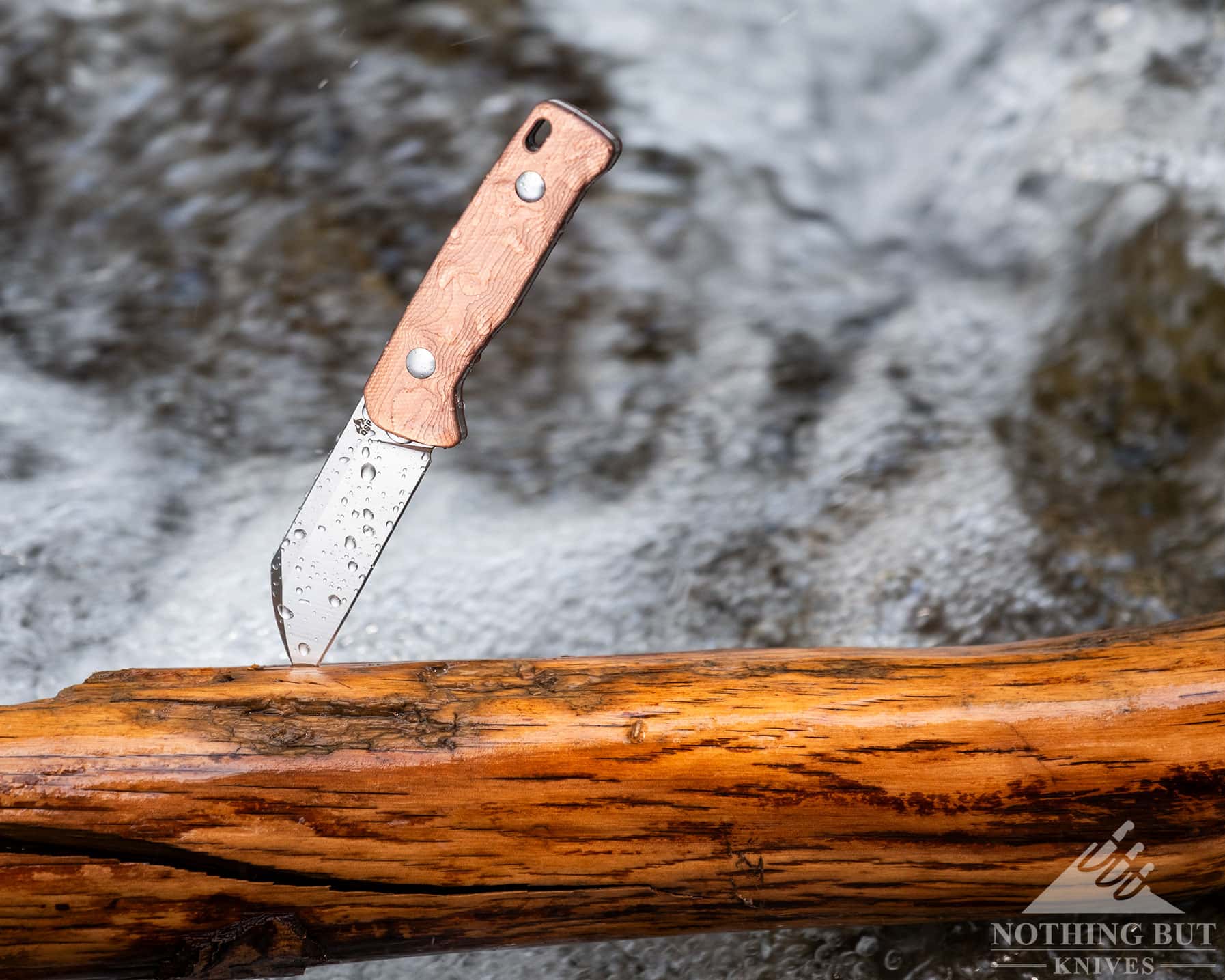 Qsp Baby Penguin Fixed Blade Review - Image 7 A small fixed blade in a wet log with a creek in the background.
