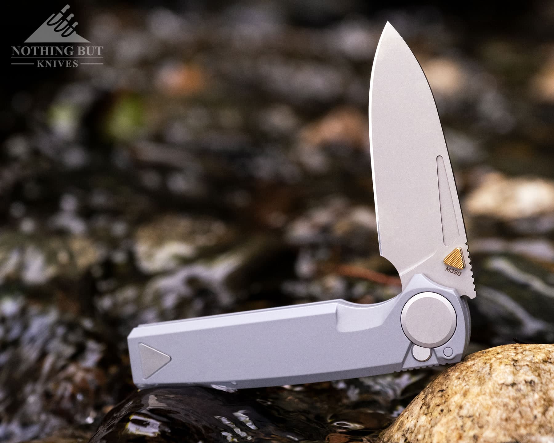 Worksharp Rmx Thumbstud Knife Review - Image 1 A close-up of the Work Sharp RMX with its blade in the half open positiom balanced on a rock on the edge of a mountain creek.